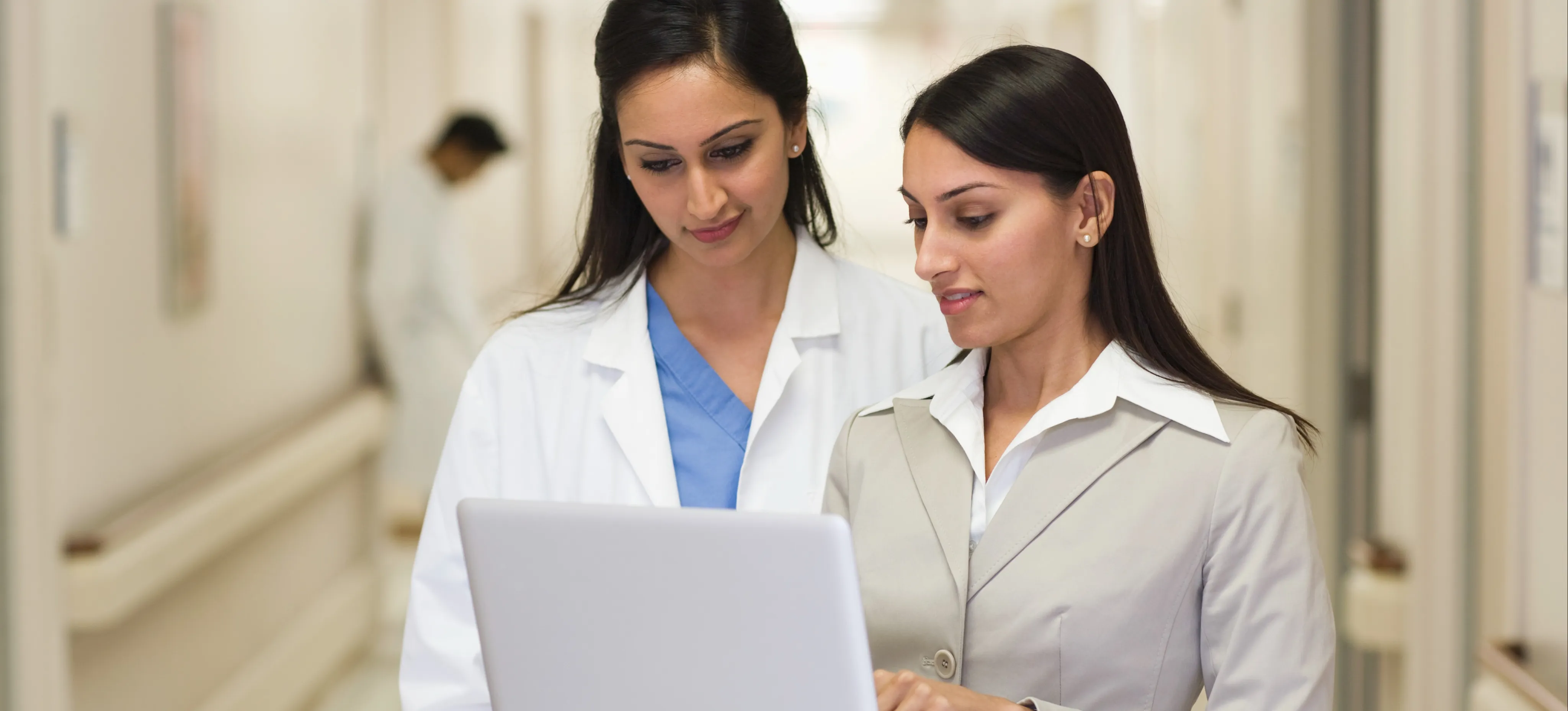 [Featured Image] A programmer shows their laptop to a doctor in a hospital to explain how they can resolve issues with an expert system in AI.