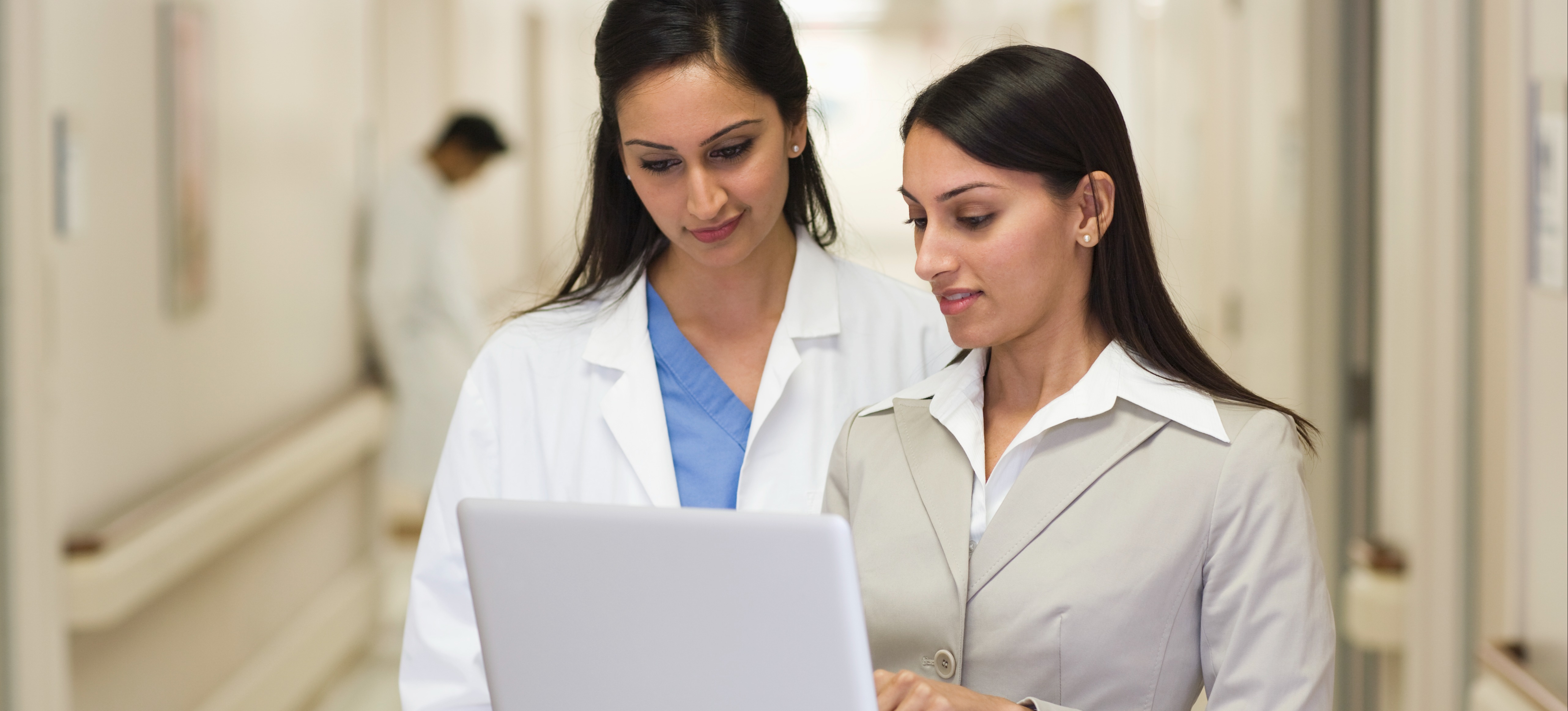 [Featured Image] A programmer shows their laptop to a doctor in a hospital to explain how they can resolve issues with an expert system in AI.