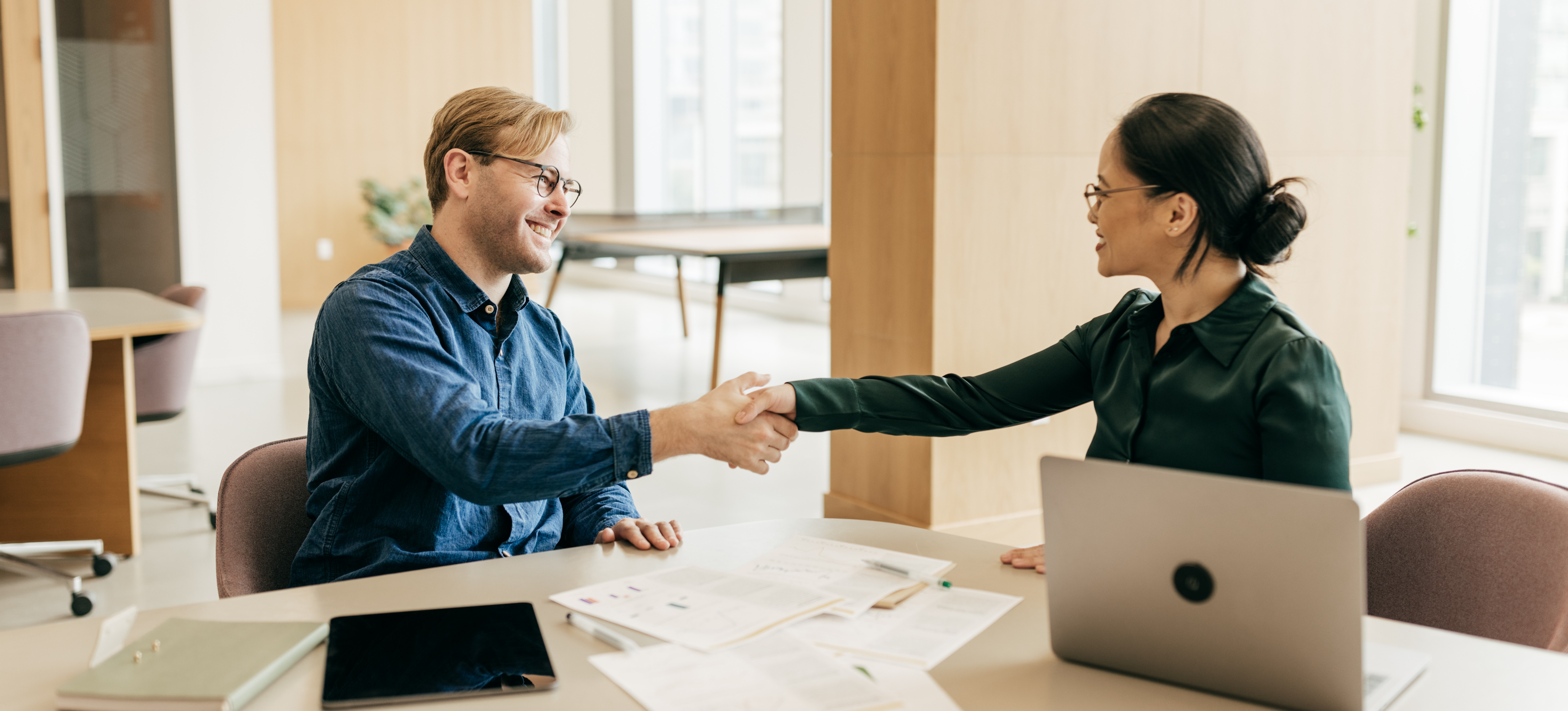 [Featured Image] A human resources manager shakes a new hire’s hand after discussing the company’s salary definition, which includes wages and benefits.