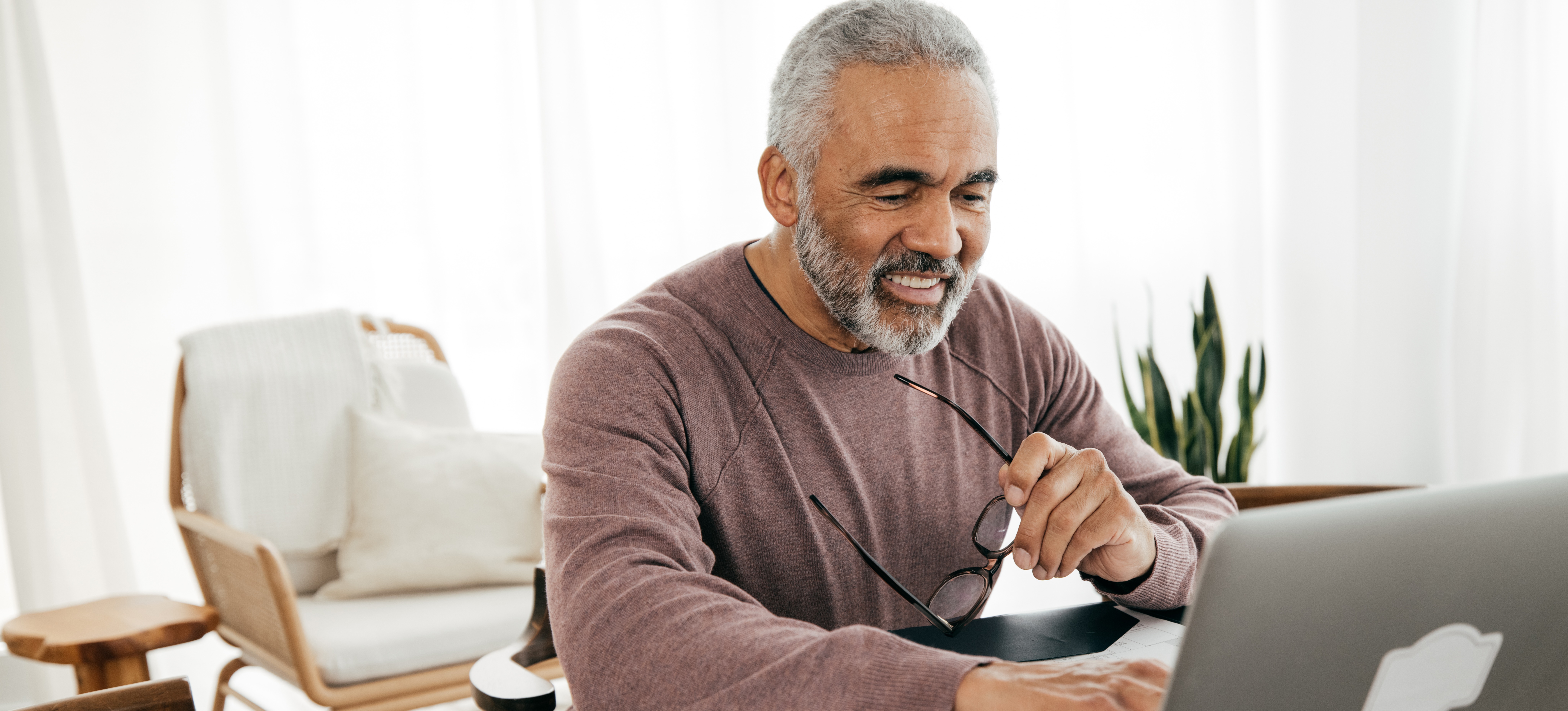 [Featured Image] A man sits at a laptop in his home office and researches what his retirement age is. 

