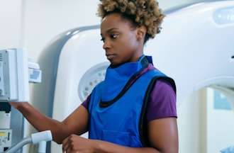 [Featured Image] A woman wearing a protective vest works with radiologic equipment. 