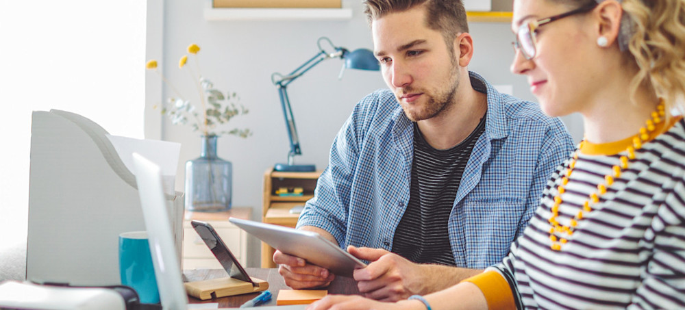 [Featured Image] An AI developer and their colleague work on a project together at a laptop in an office. 