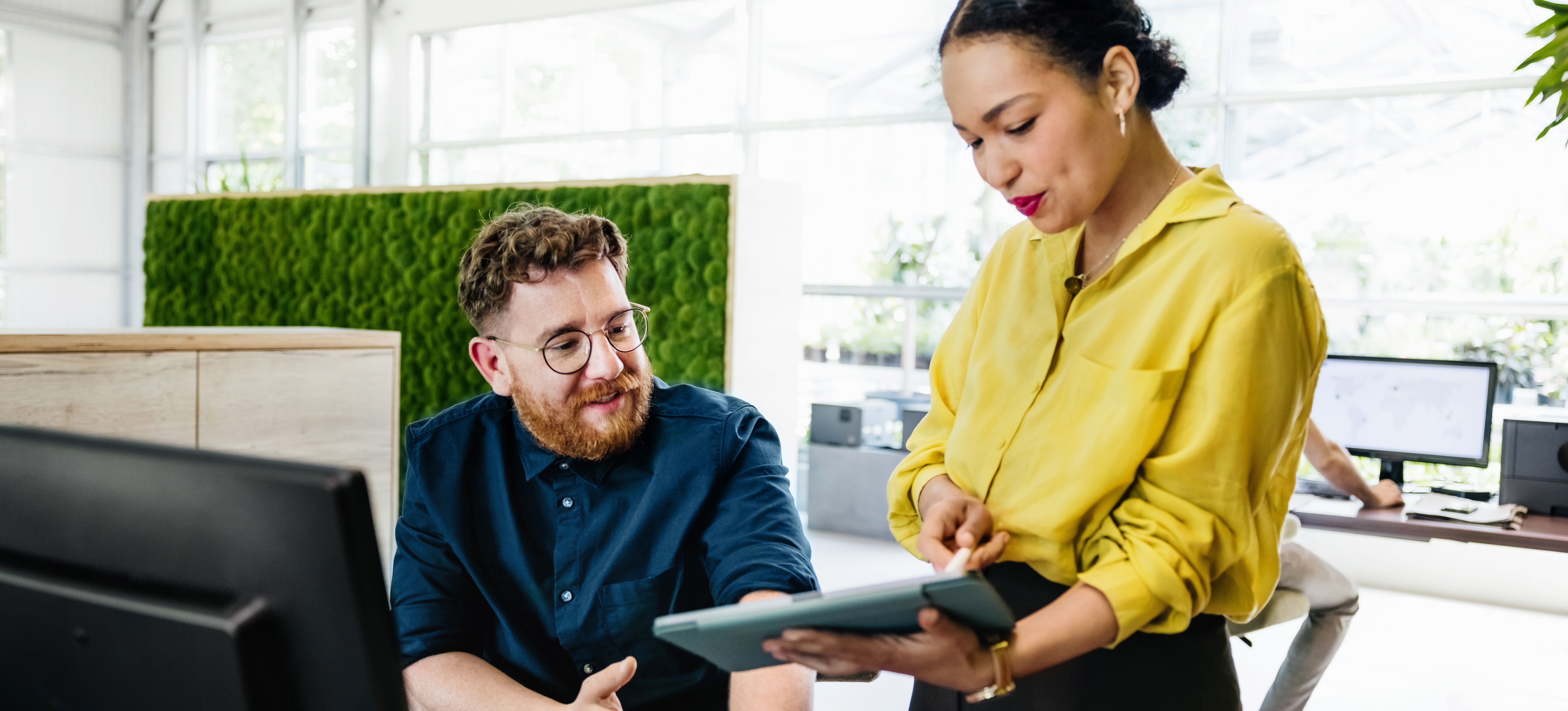 [Featured Image] Two colleagues look at a tablet while one explains the program-aided language models used to create a solution. 
