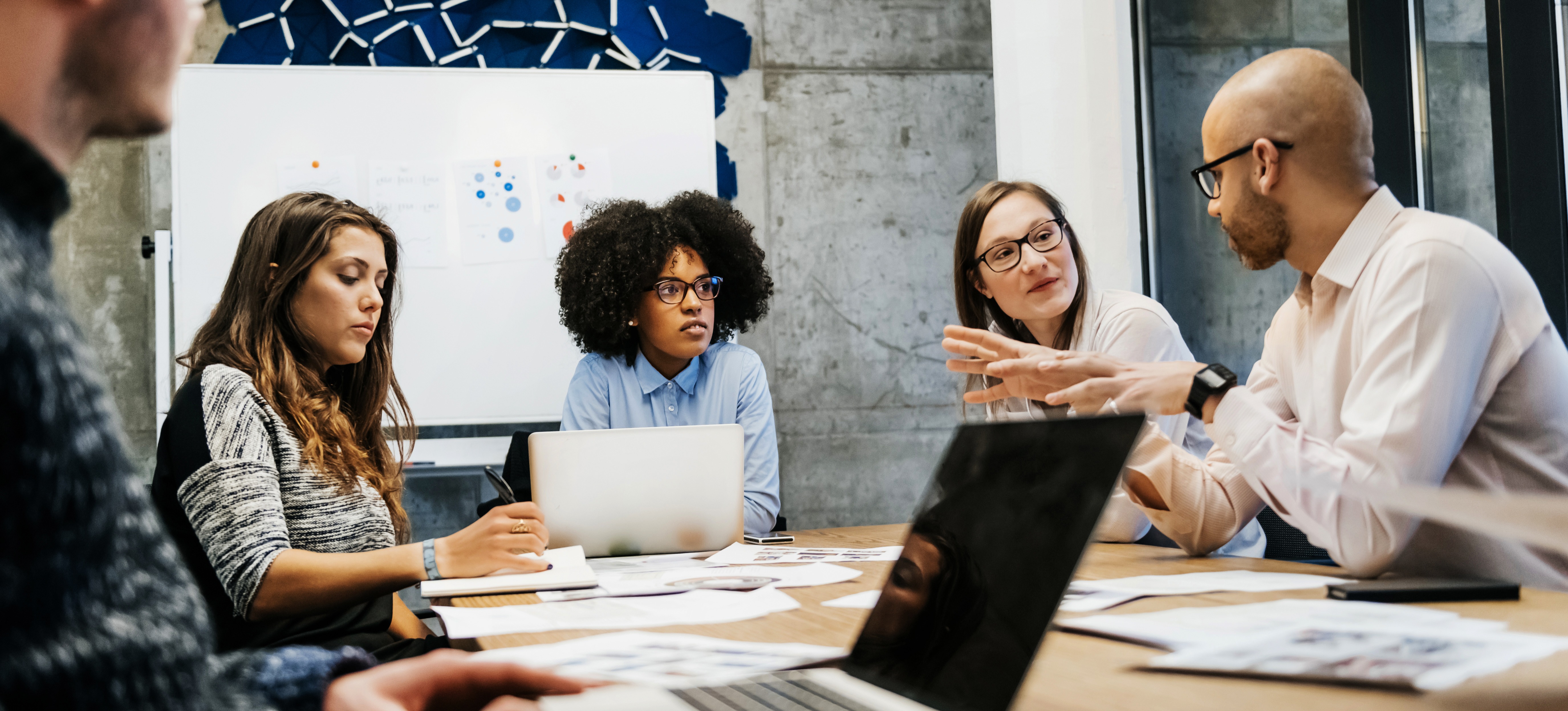 [Featured Image] A compliance analyst listens to another team member discuss business processes in a team meeting designed to provide solutions.
