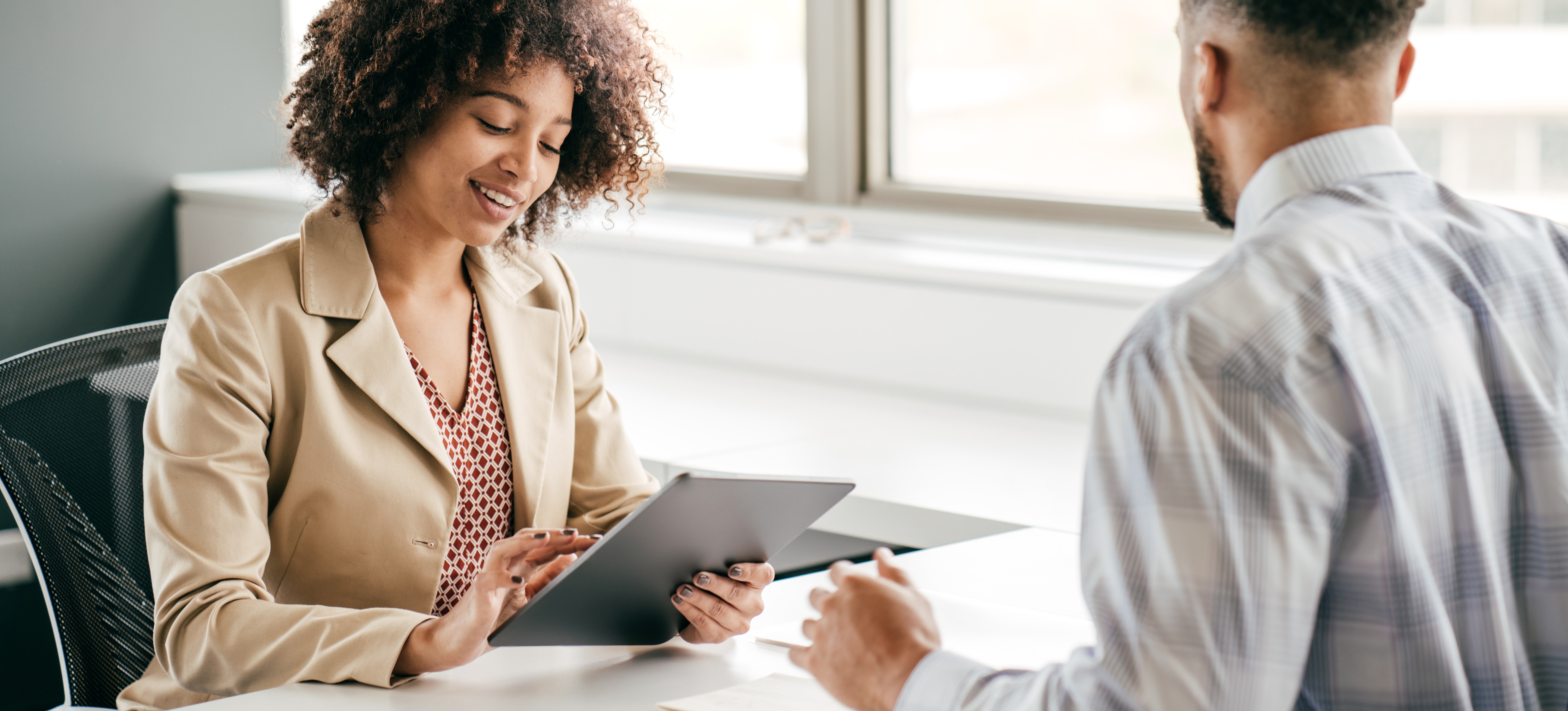 [Featured Image] A recruiter engaging with a candidate during an interview in a professional environment, holding a tablet, and smiling while discussing predictive analytics interview questions.
