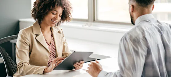 [Featured Image] A recruiter engaging with a candidate during an interview in a professional environment, holding a tablet, and smiling while discussing predictive analytics interview questions.
