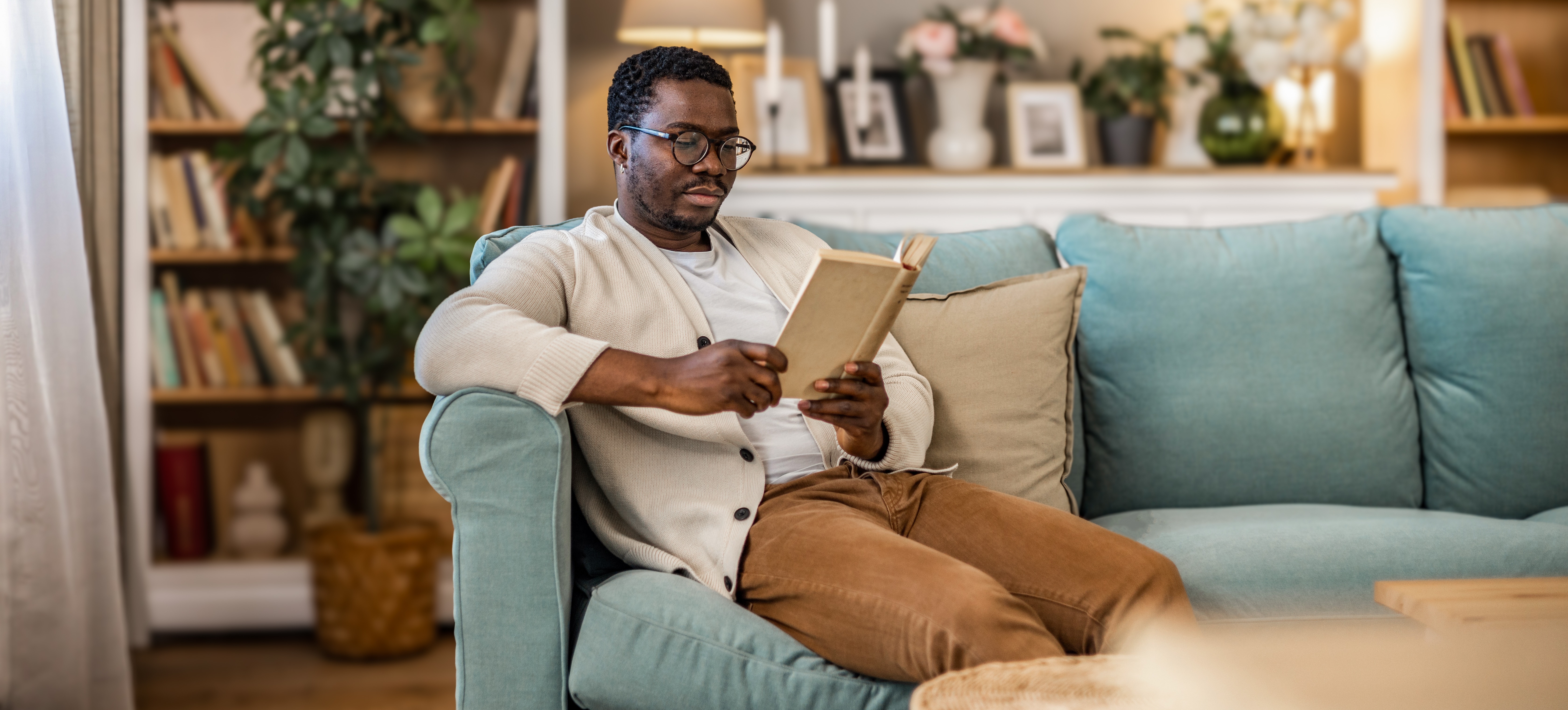 [Hauptbild] Ein Mann sitzt gemütlich auf einem Sofa in einem schön eingerichteten Wohnzimmer und liest ein Buch.