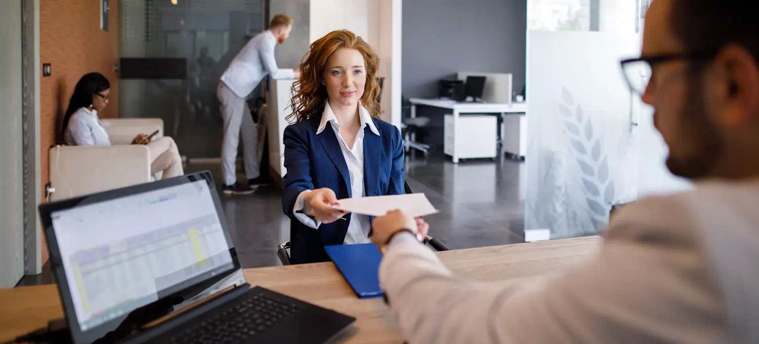 [Featured image]: A job applicant hands their front-end developer resume to a manager seated behind a desk.
