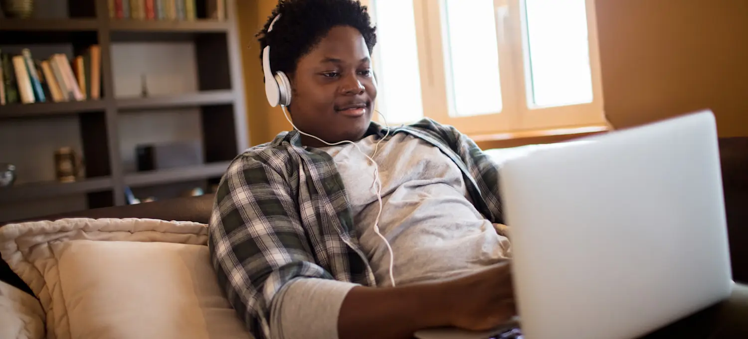 [Featured image] A person in a plaid shirt wears headphones and works on their Associate of Science degree on their laptop.
