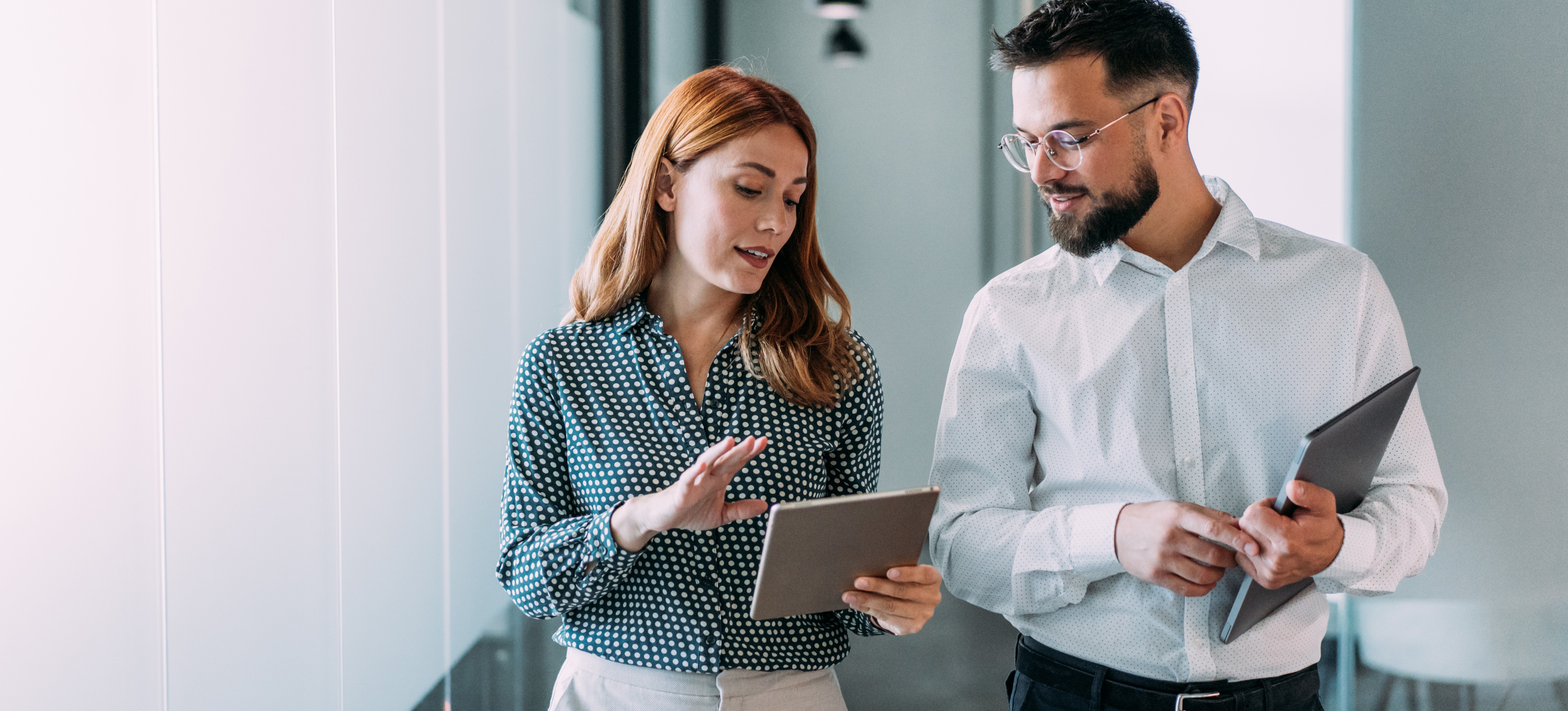 [Hauptbild] Ein Manager geht mit einem Mitarbeiter durch ein Büro, während beide auf ein Tablet schauen und einen Plan zur Leistungsverbesserung besprechen.