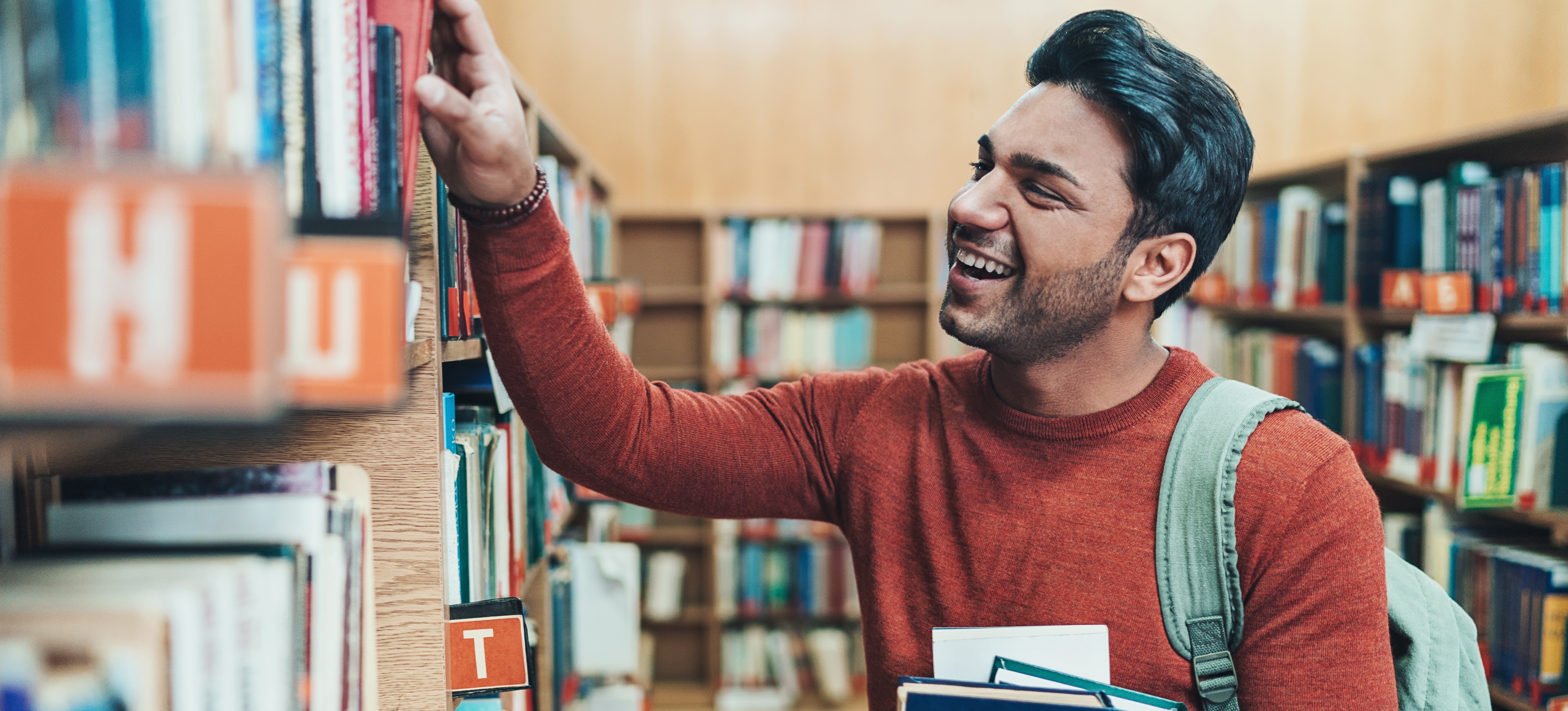[Featured Image] An undergraduate student looks for books in the library to use for his final year project. 