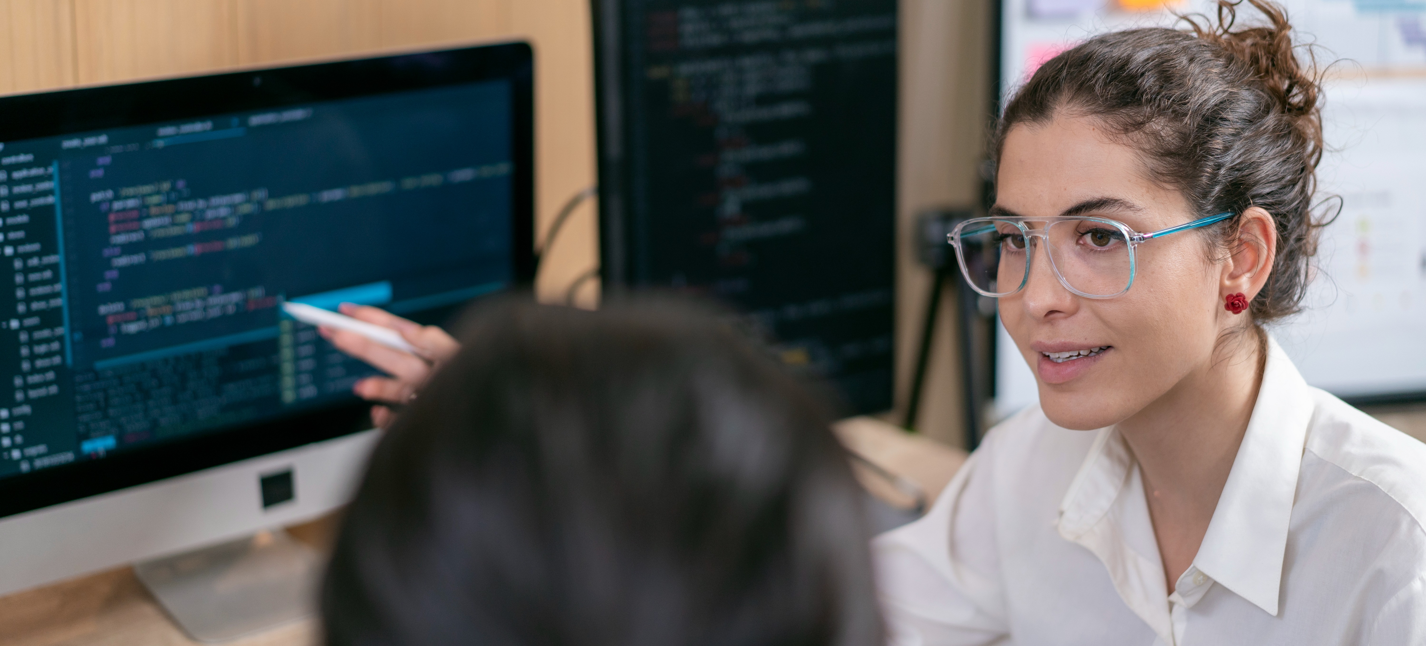 [Featured Image] Python professionals in a work environment discussing how to improve Python coding skills while reviewing code on their computers.
