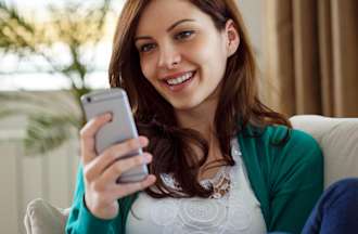 [Featured Image] A woman sitting on a couch uses a smartphone to interact with a chatbot that uses natural language generation.  