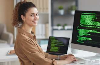 [Featured image] A developer in a light brown shirt sits at a desk learning a front-end programming language on a computer monitor connected to a laptop and tablet.