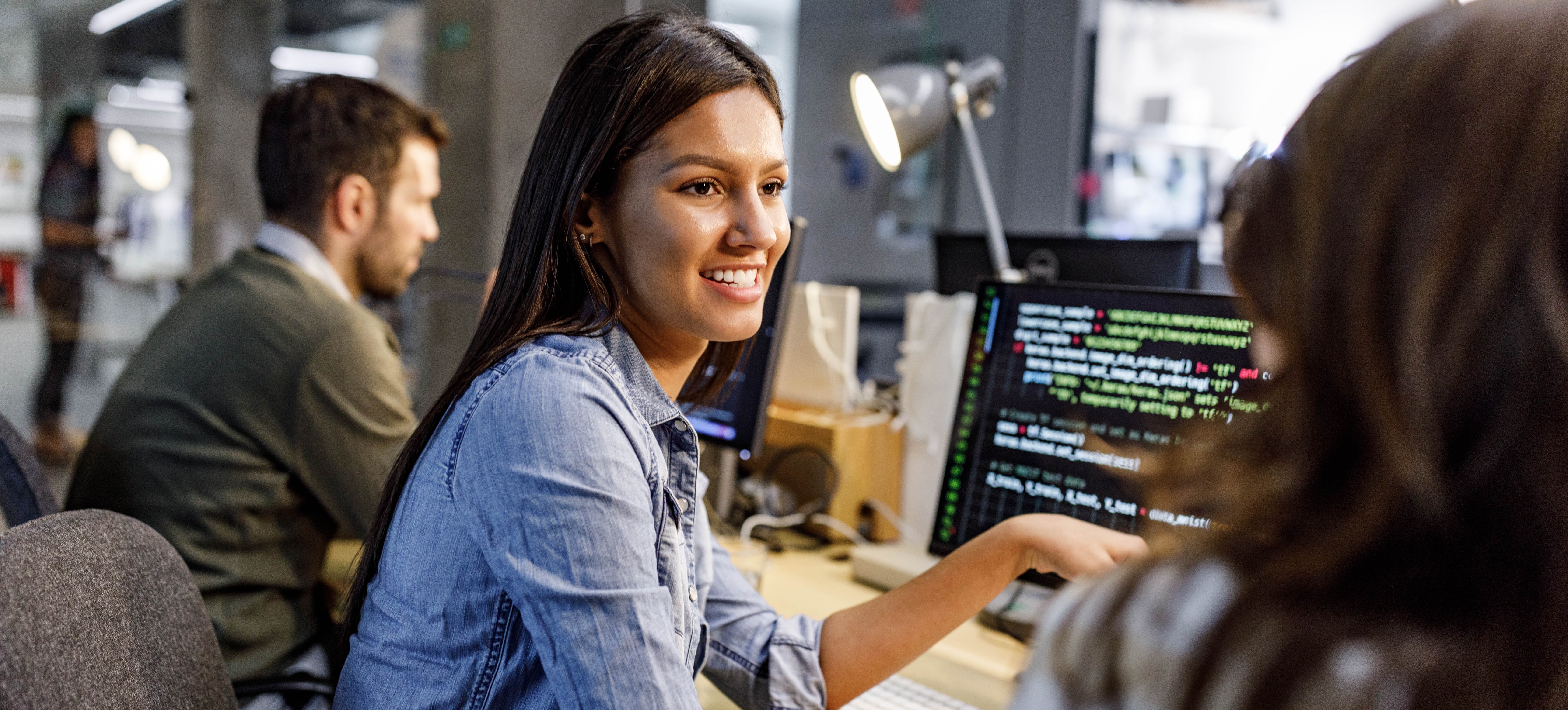 [Image en vedette] Un programmeur souriant est assis devant son ordinateur et parle avec un collègue de missions de programmation.
