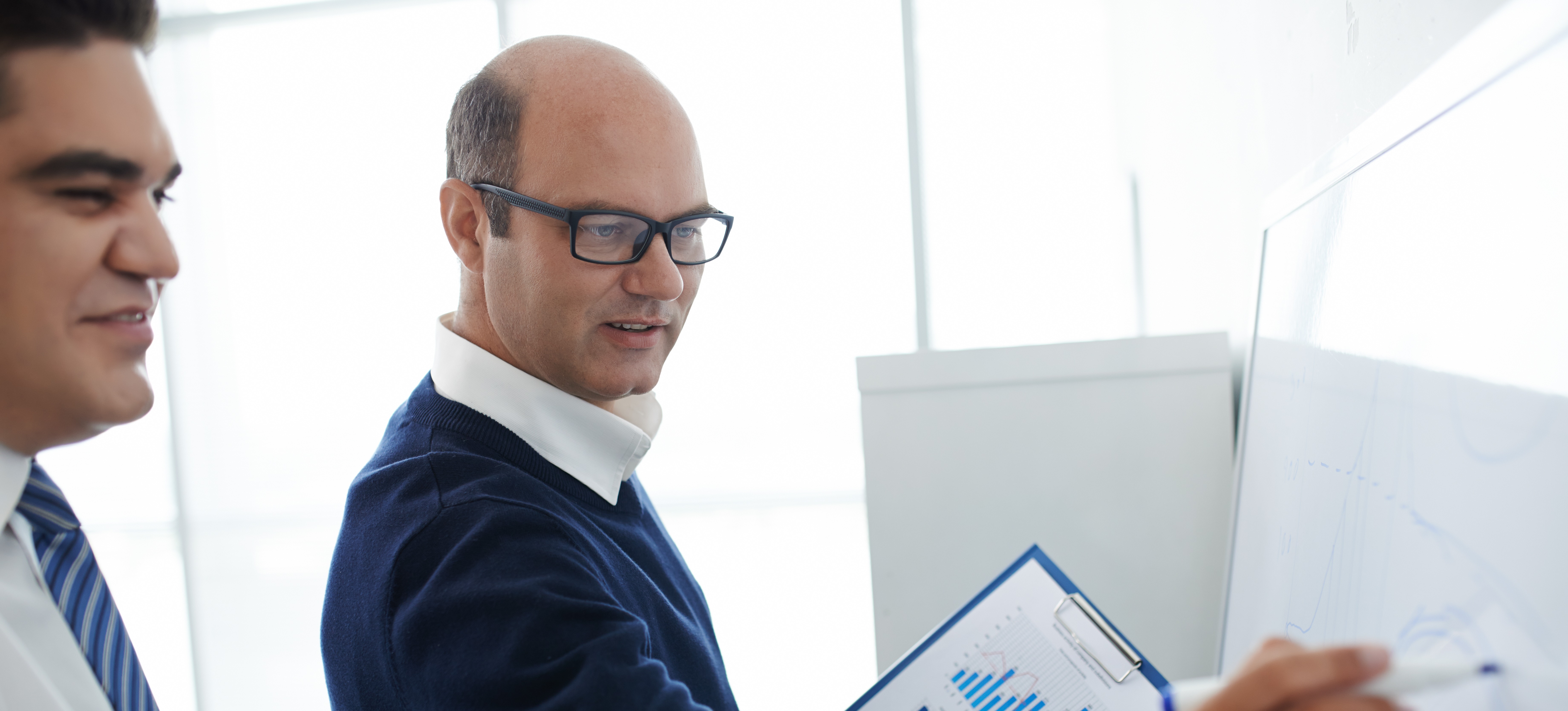 [Featured image] A product coordinator, wearing a blue sweater, white shirt, and glasses, is conducting a meeting with their team. 