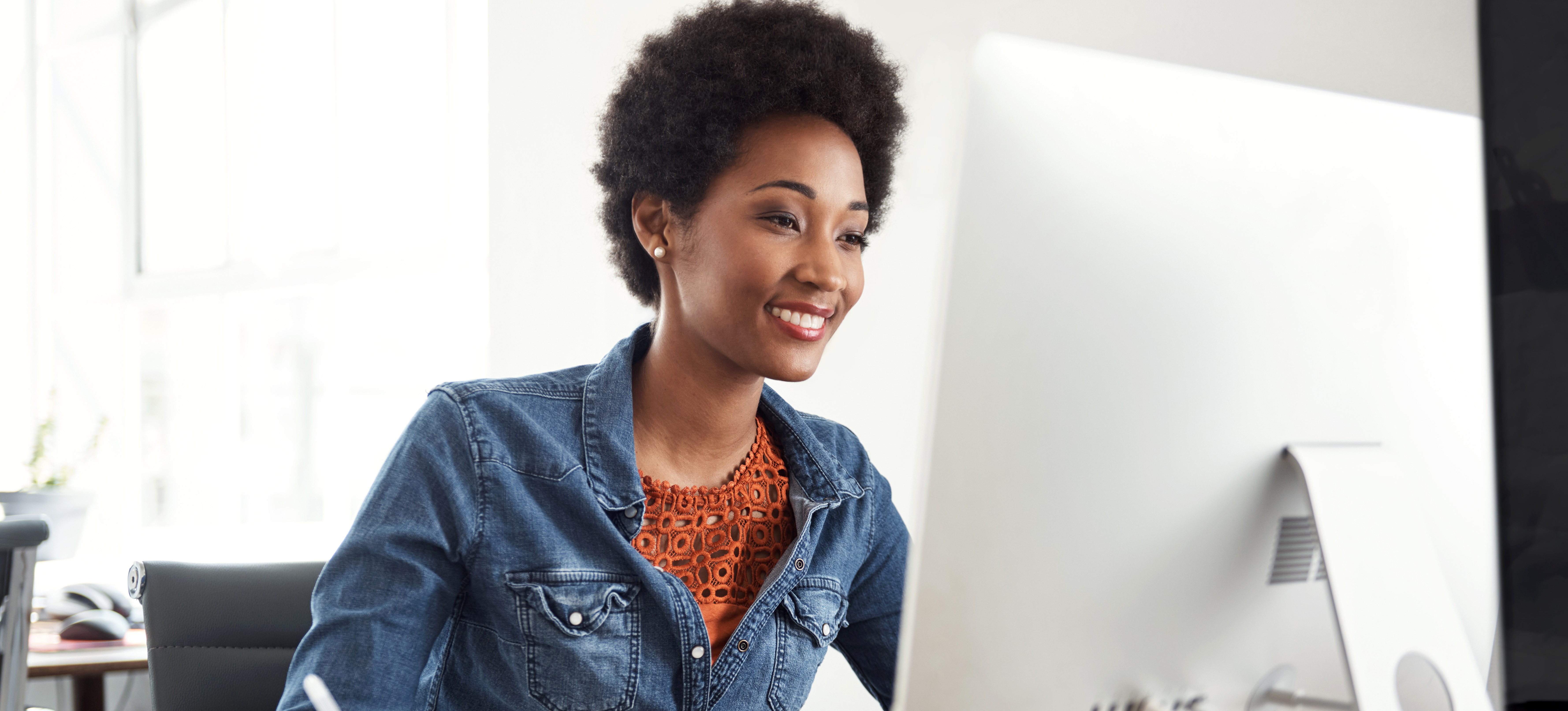 [Featured Image] A smiling professional dressed in denim using an email marketing strategy holds a pen above a journal and looks at their computer screen.