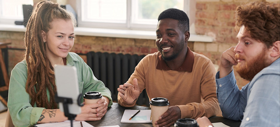 [Featured Image] Three marketing specialists are discussing their AI for influencer marketing strategies while sitting at a workspace together and talking with a colleague via video.
