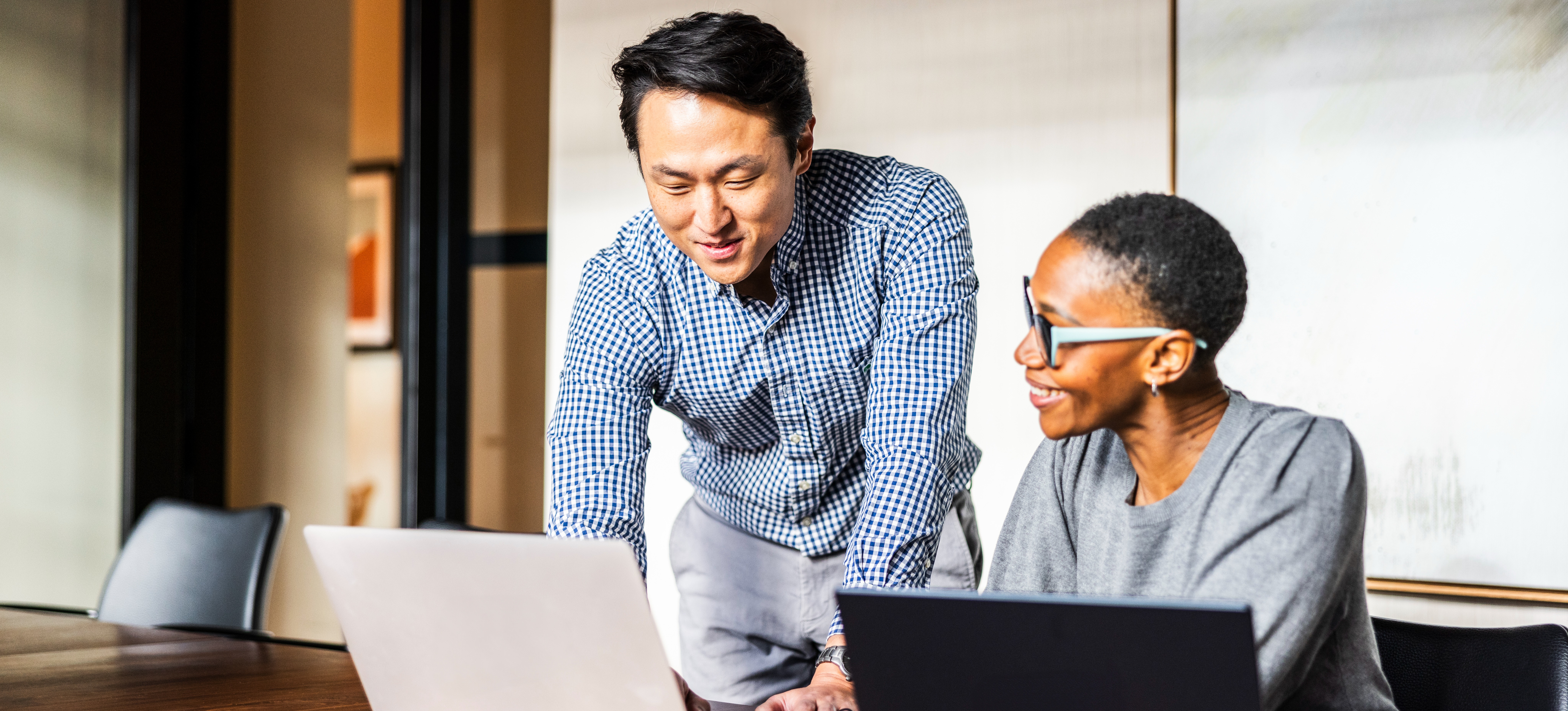 [Feature Image] After learning how to conduct a root cause analysis, two colleagues review the results on their laptops as they devise a strategy to solve a business problem. 
