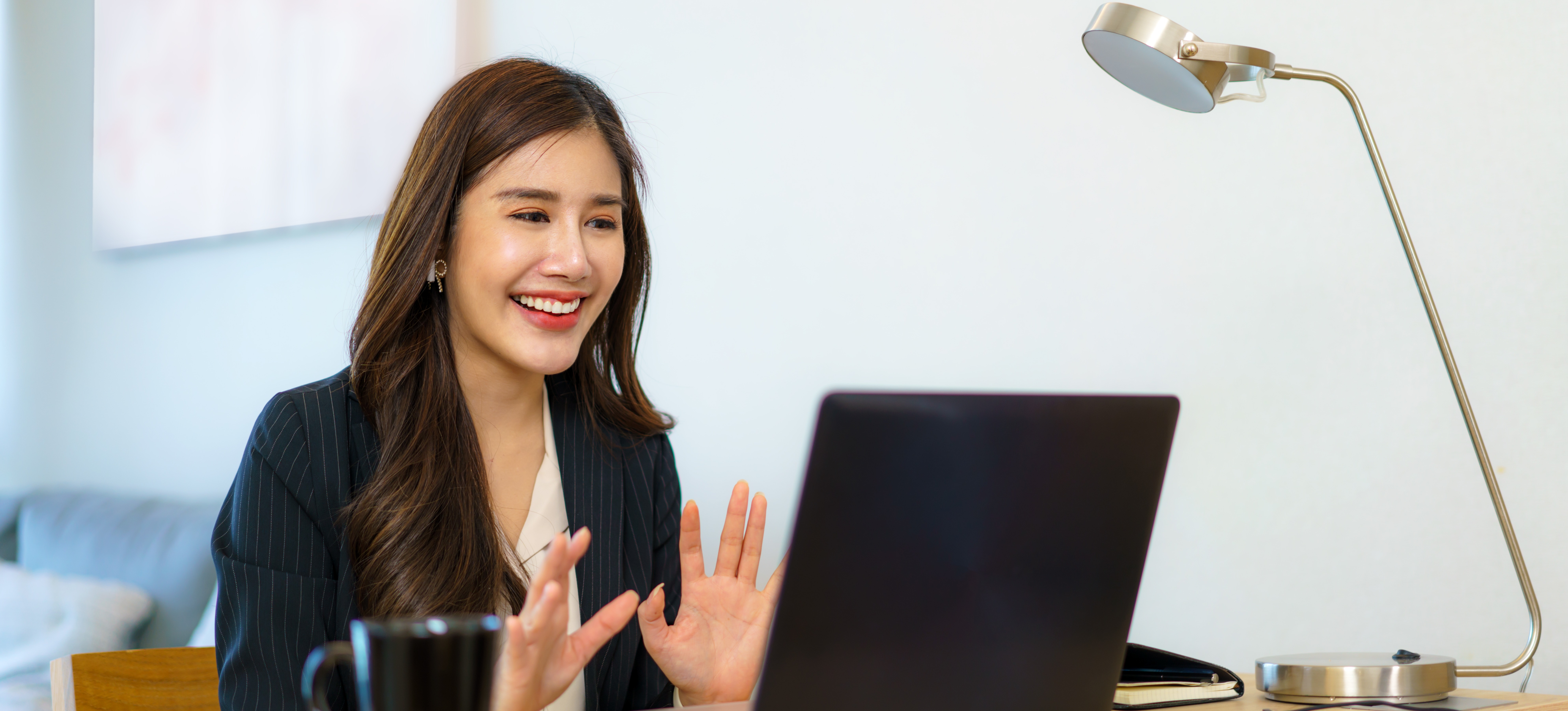 [Featured Image] Women sits at her desk at home on her laptop. She is smiling while answering HireVue interview questions.