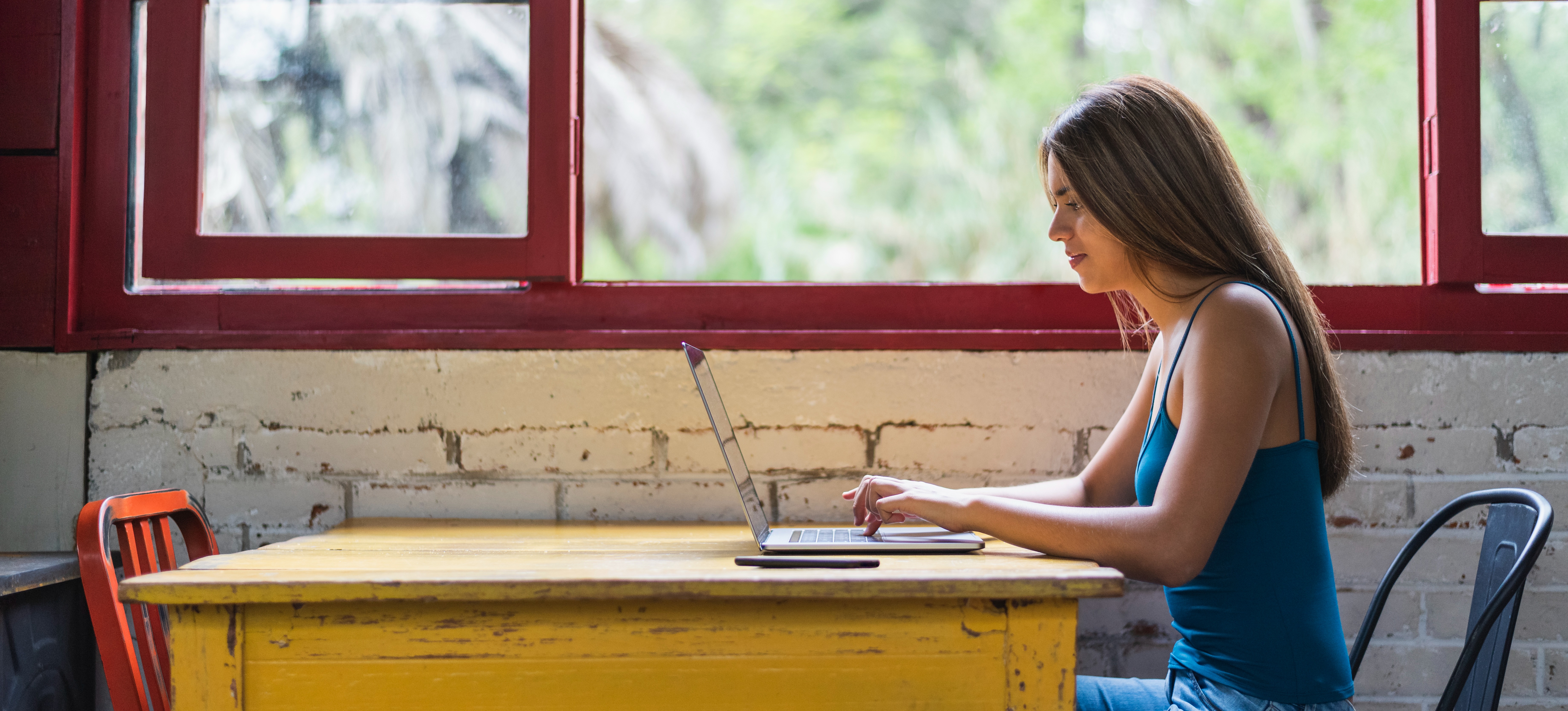 [Featured Image] A woman uploading her resume to LinkedIn on her laptop in a café.