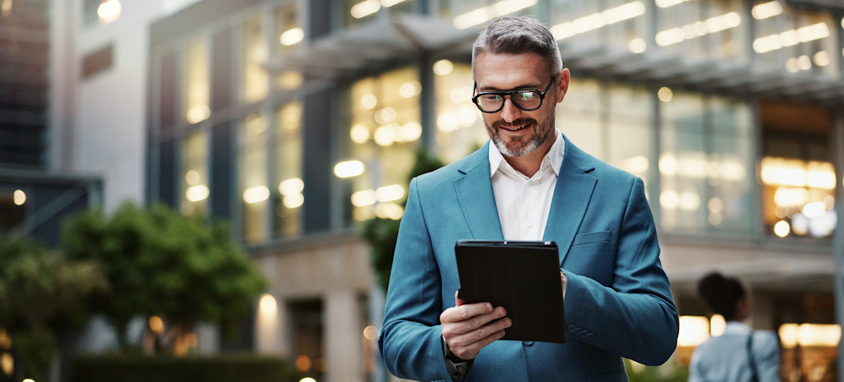 [Featured Image] A business person stands outside an office building in a blazer and researches important social media platforms for companies on their tablet.
