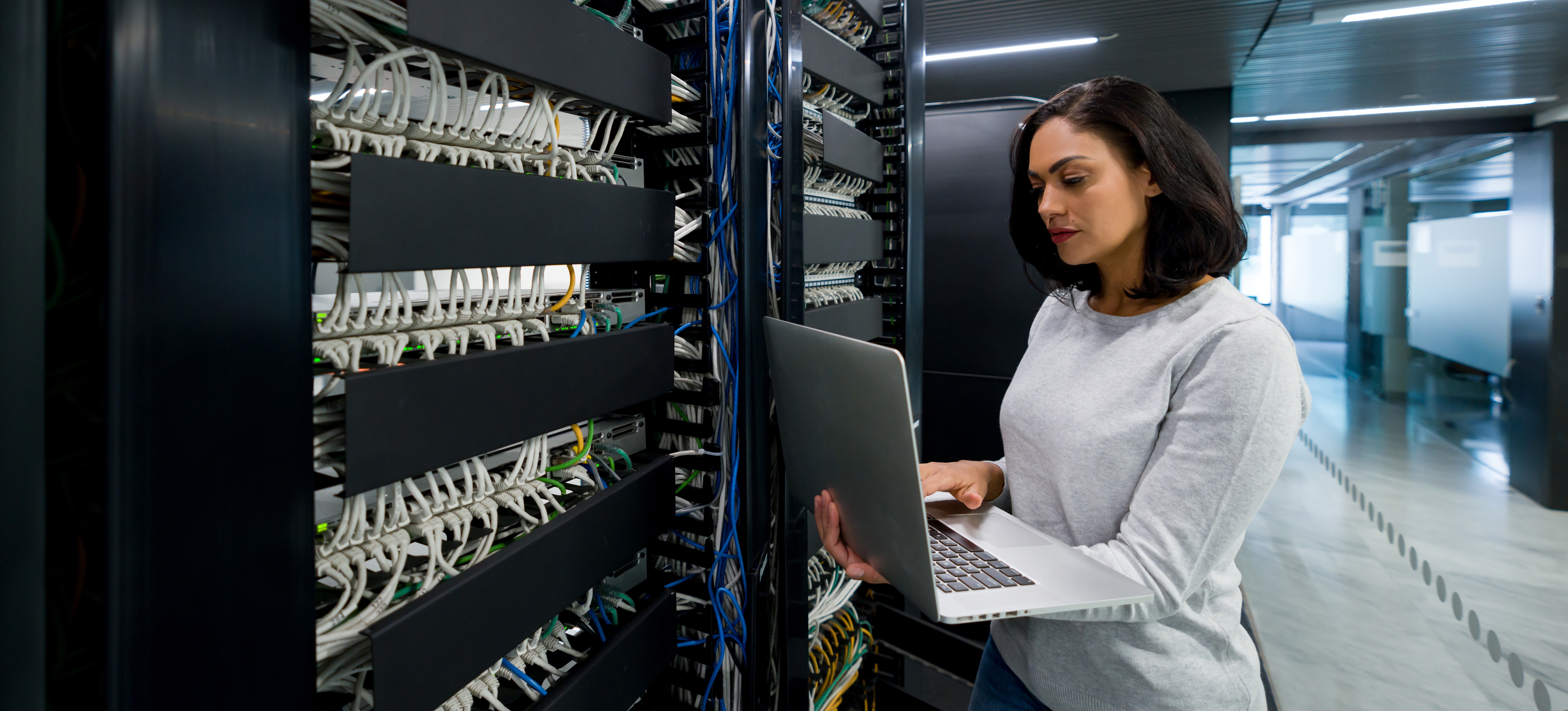 [Featured Image] An IT professional stands in a server room with their laptop and uses their computer engineering skills to troubleshoot issues with the hardware.
