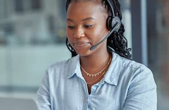 [Featured Image] A woman wearing a headset is on her laptop and answers phones at an IT call center.
