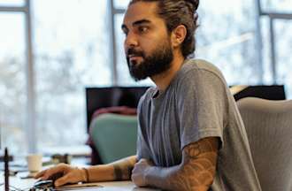 [Featured image] A data analyst works with a database on a desktop computer in an office with big windows.