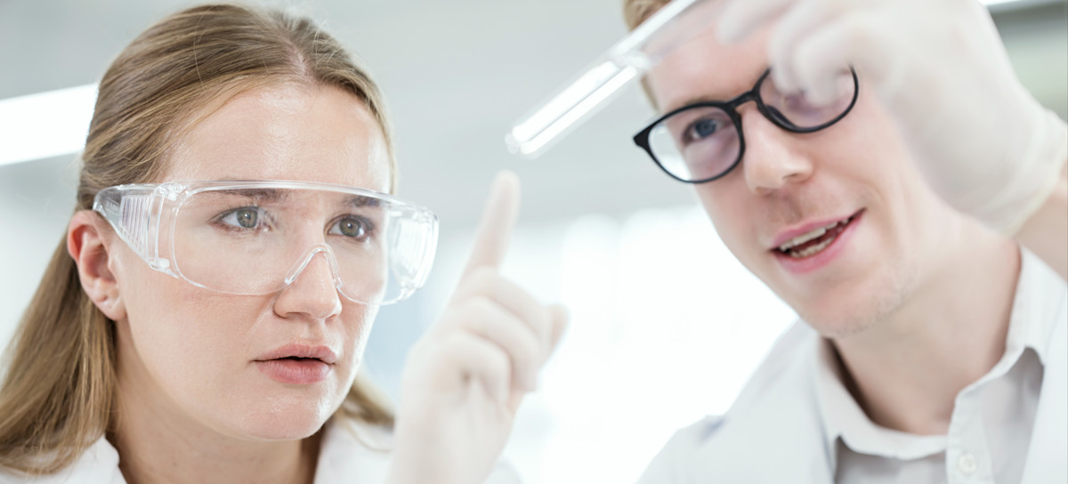 [Featured Image] Two medical technologists examine a test tube in a lab while earning a competitive salary.  