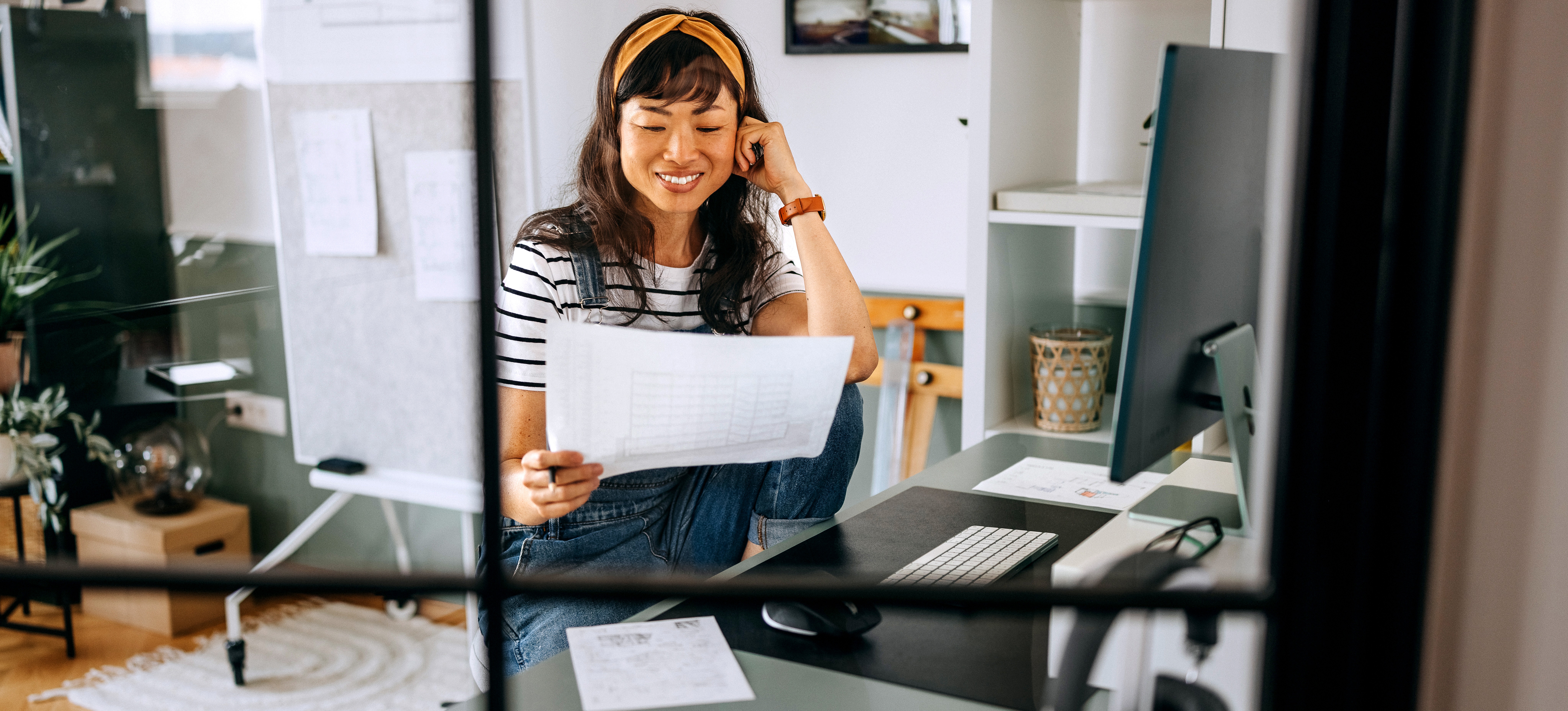 [Featured Image] A casually dressed businesswoman is in her home office, working remotely, reviewing weekly numbers for her team.
