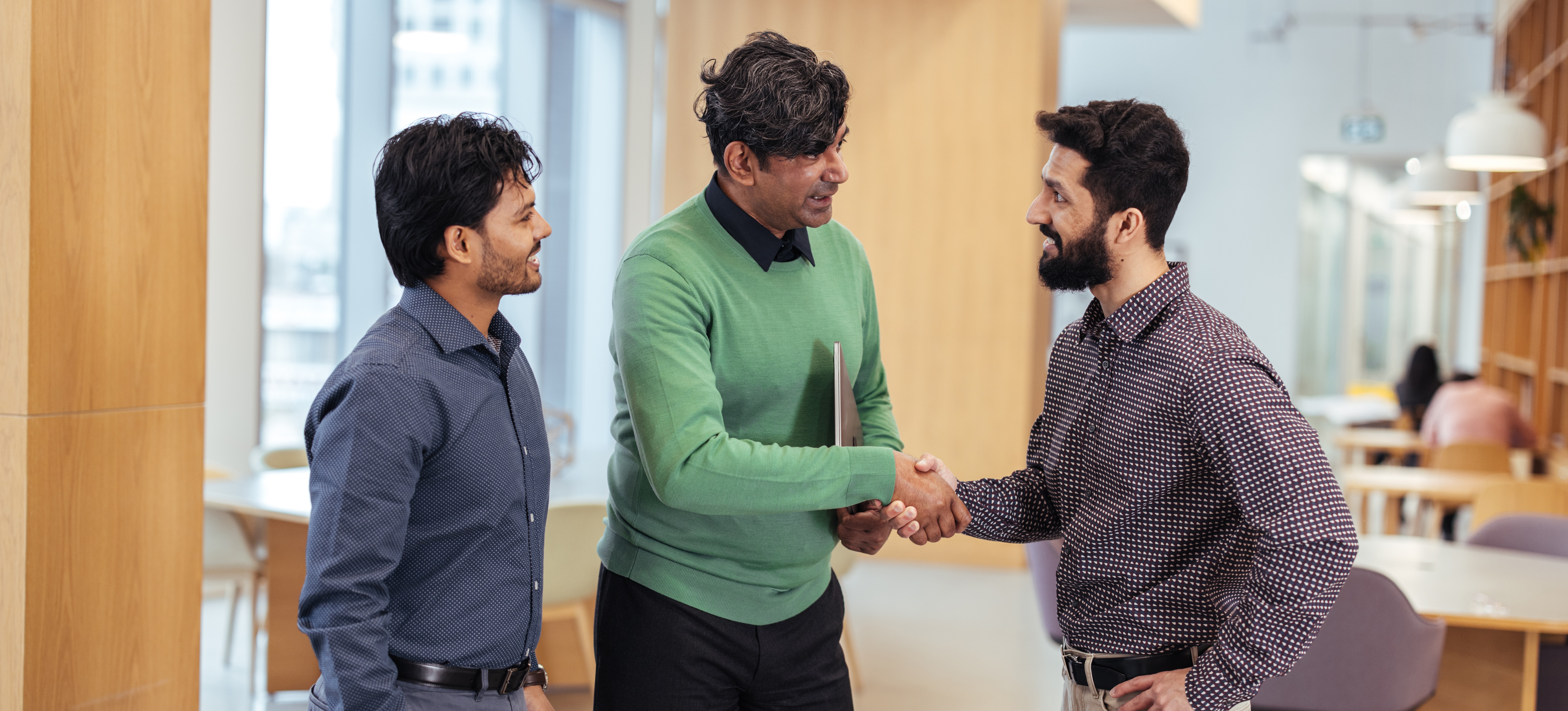 [Featured Image] A SHRM-certified human resources manager shakes hands with an employee in an office setting as another smiling employee looks on.