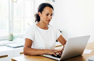 [Featured image] A woman works on her laptop at home, preparing to earn the TOGAF certification.
