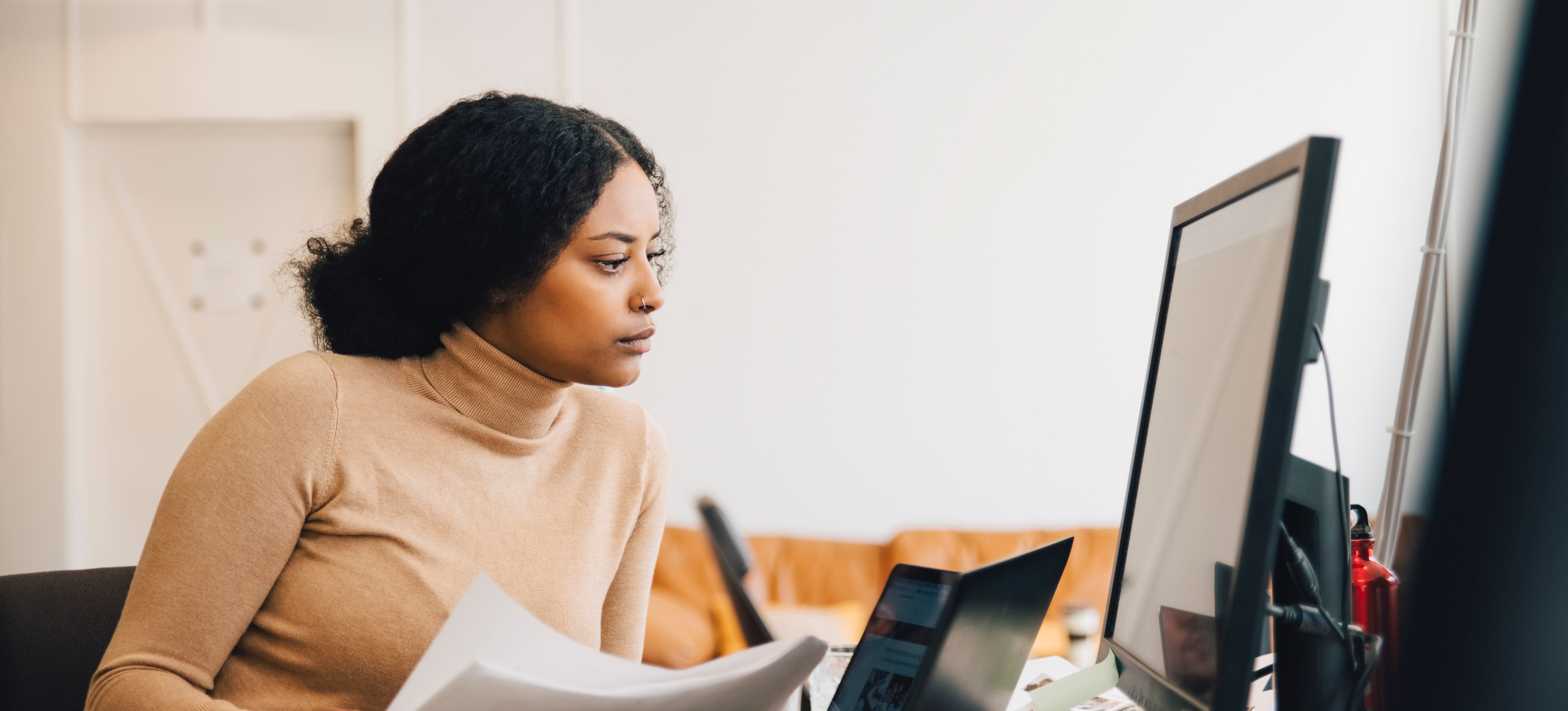 [Feature Image] An aspiring computer professional studies JSON vs. XML as they complete their coursework on a desktop computer with two laptops also open on their desk.