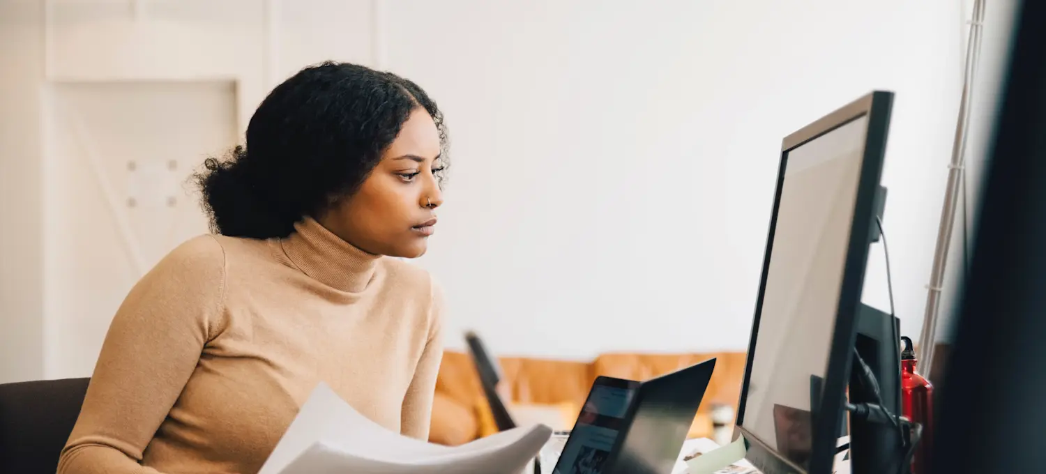 [Feature Image] An aspiring computer professional studies JSON vs. XML as they complete their coursework on a desktop computer with two laptops also open on their desk.