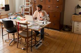 [Featured image] A parent sits at a desk holding a baby while working.