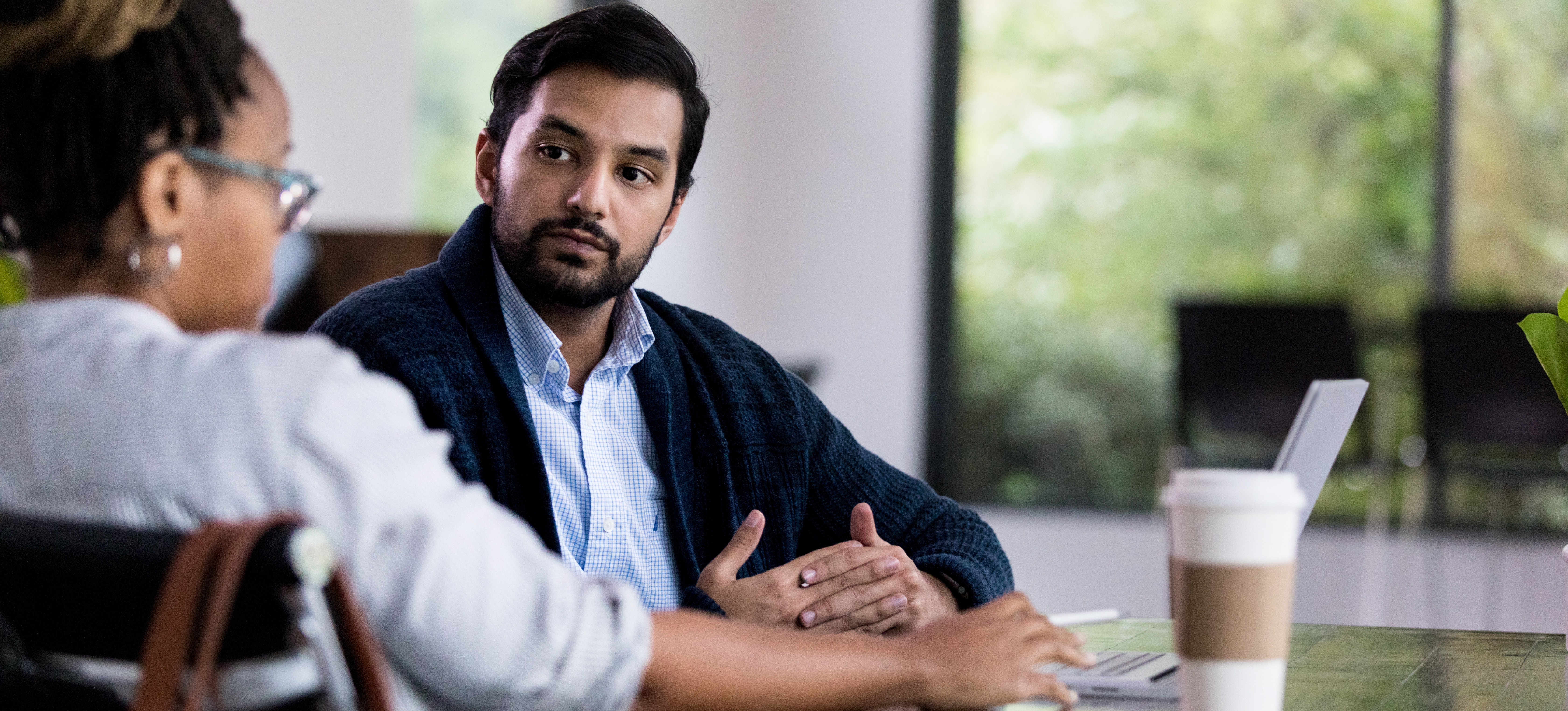[Featured Image] Two colleagues, one male and one female, sit at a table discussing "What is equity in the workplace?" at the office.
