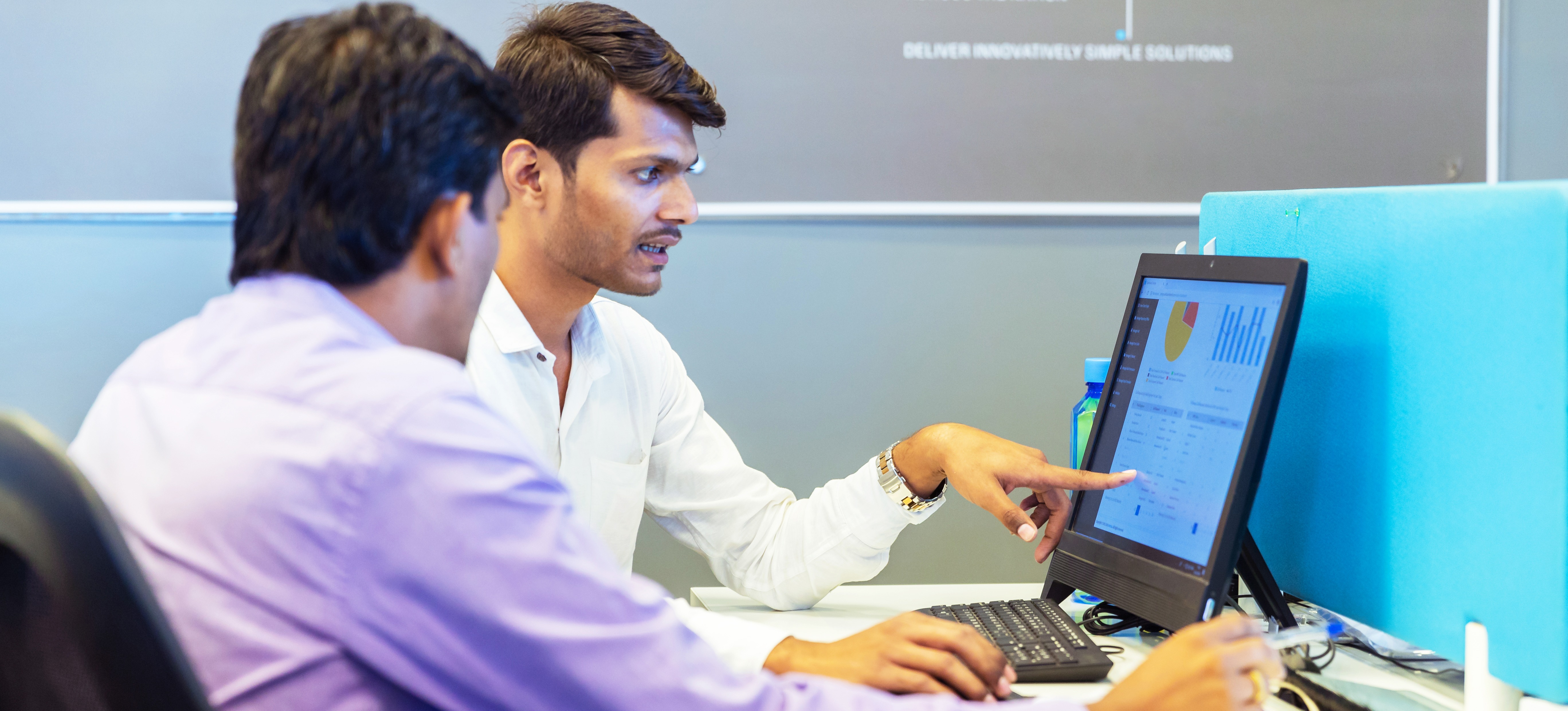 [Featured Image]: Two professionals look at a computer as they discuss data warehouse vs database to store and manage data.

