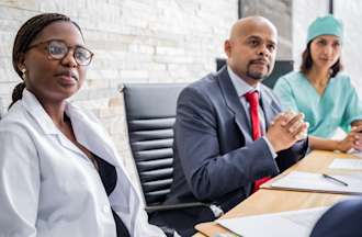 [Featured Image] A hospital administrator and two medical professionals sit at a conference table.