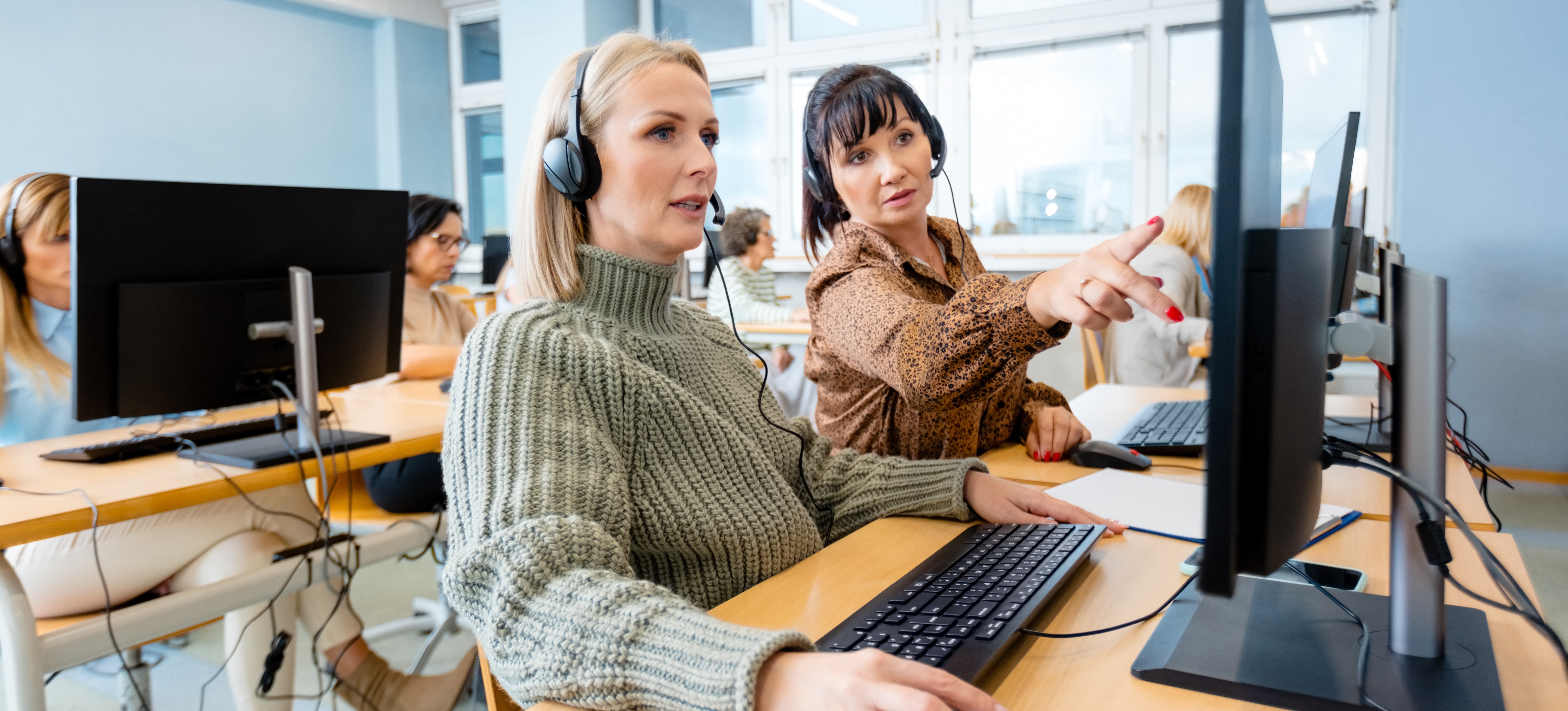 [Image en vedette] Deux collègues portant des écouteurs et assis devant des ordinateurs suivent des cours en ligne dans le cadre de la stratégie de perfectionnement professionnel de leur entreprise.