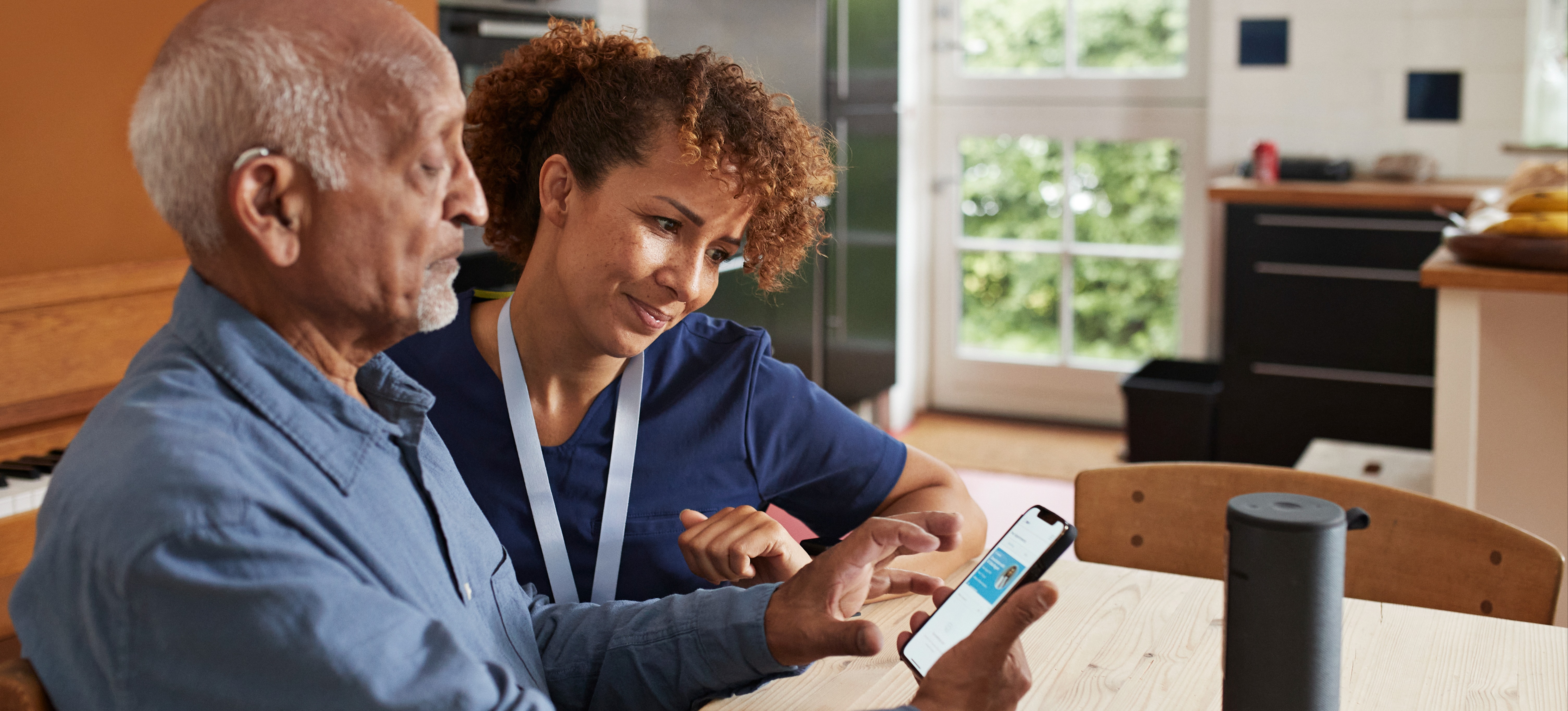 [Featured Image] A nurse is at a patient's home showing them how to use a new doctor-patient communication app developed using AI.
