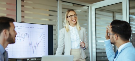 [Featured Image]  A marketer in a business suit presents a go-to-market strategy to their team in a conference room.