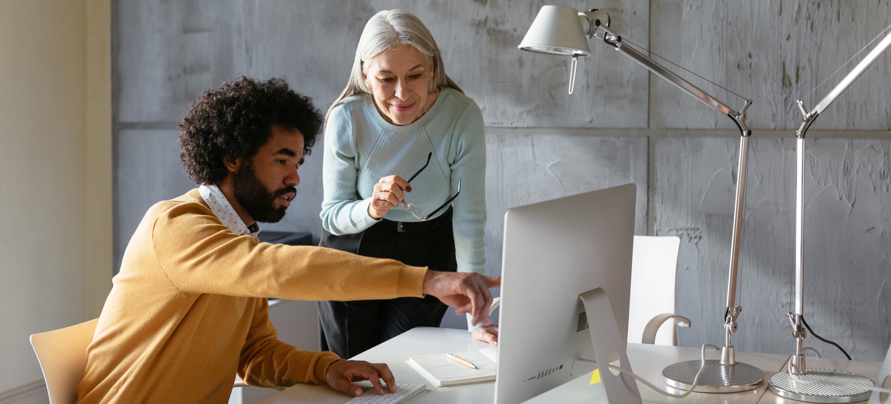 [Featured image] A person in a blue shirt talks with their business partner, a person in a yellow sweater, about their business structure. 