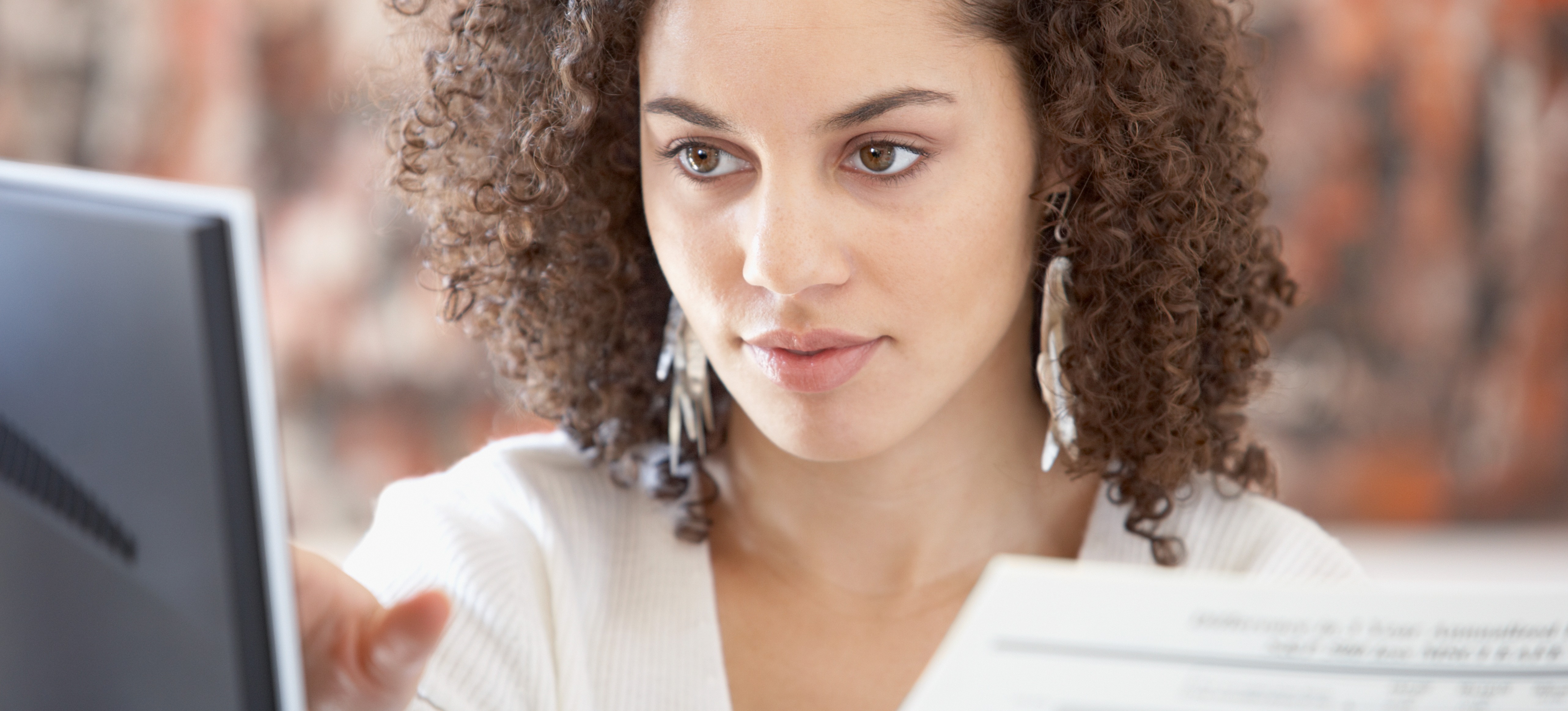 [Featured Image] A data analyst looks at her computer monitor and holds a graph as she studies data using logistic regression.