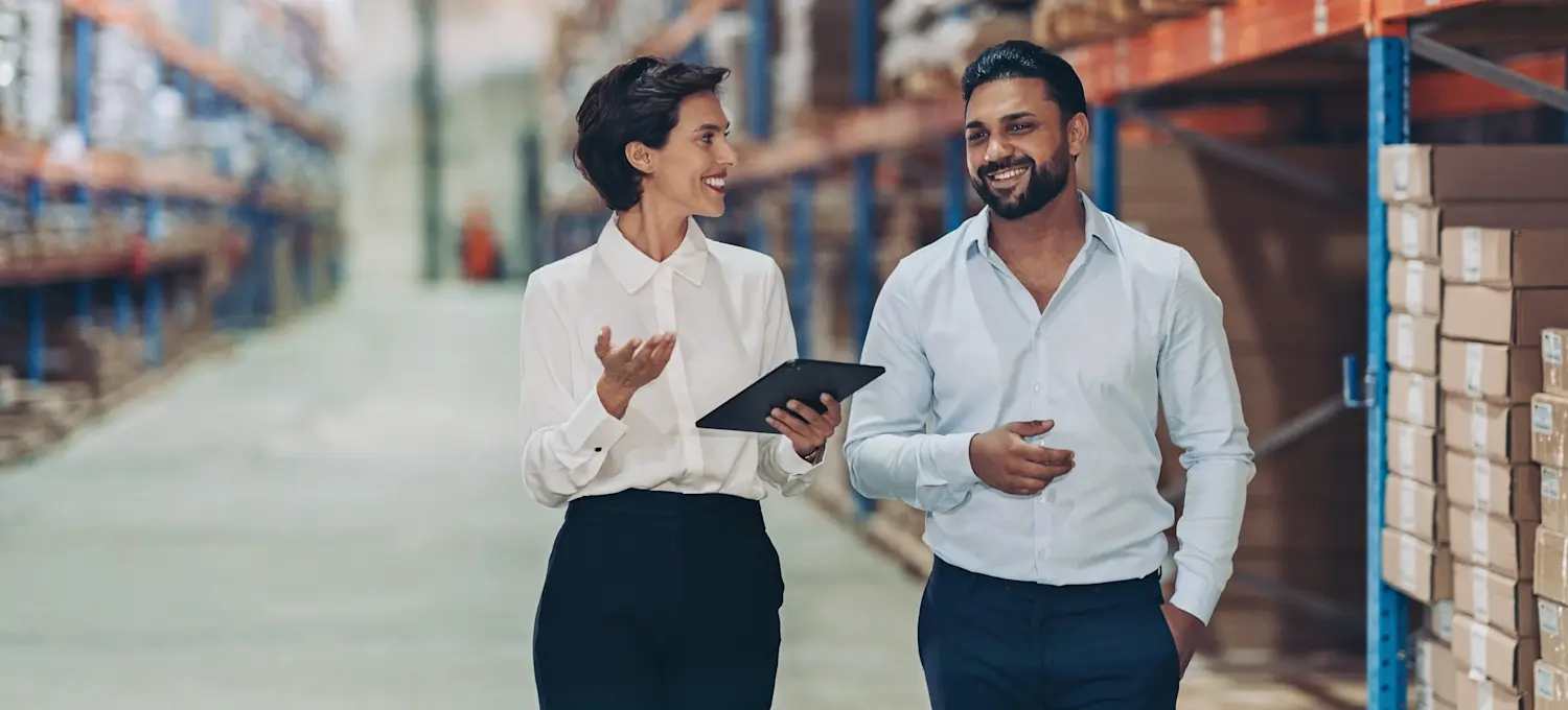 [Featured Image] A businessperson is walking in a warehouse with a colleague who just received a promotion to warehouse manager after receiving their CLTD certification.