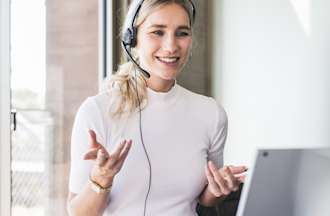 [Featured image] A sustainability analyst sits at a laptop and wears a headset while consulting with a business owner about how to improve the company's environmental impact. 