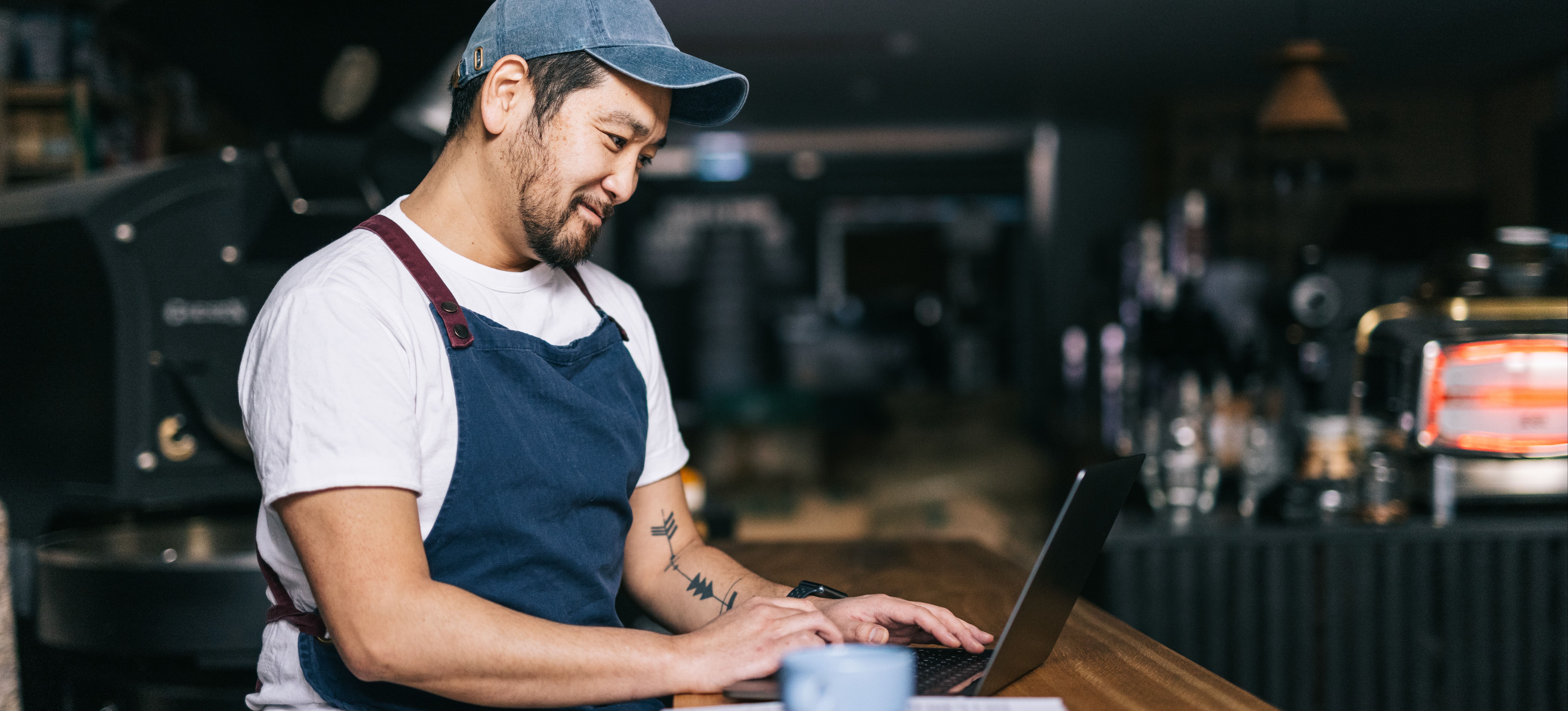 [Featured Image] A small business owner sits in their shop and sets up a display campaign in Google Ads with their laptop.
