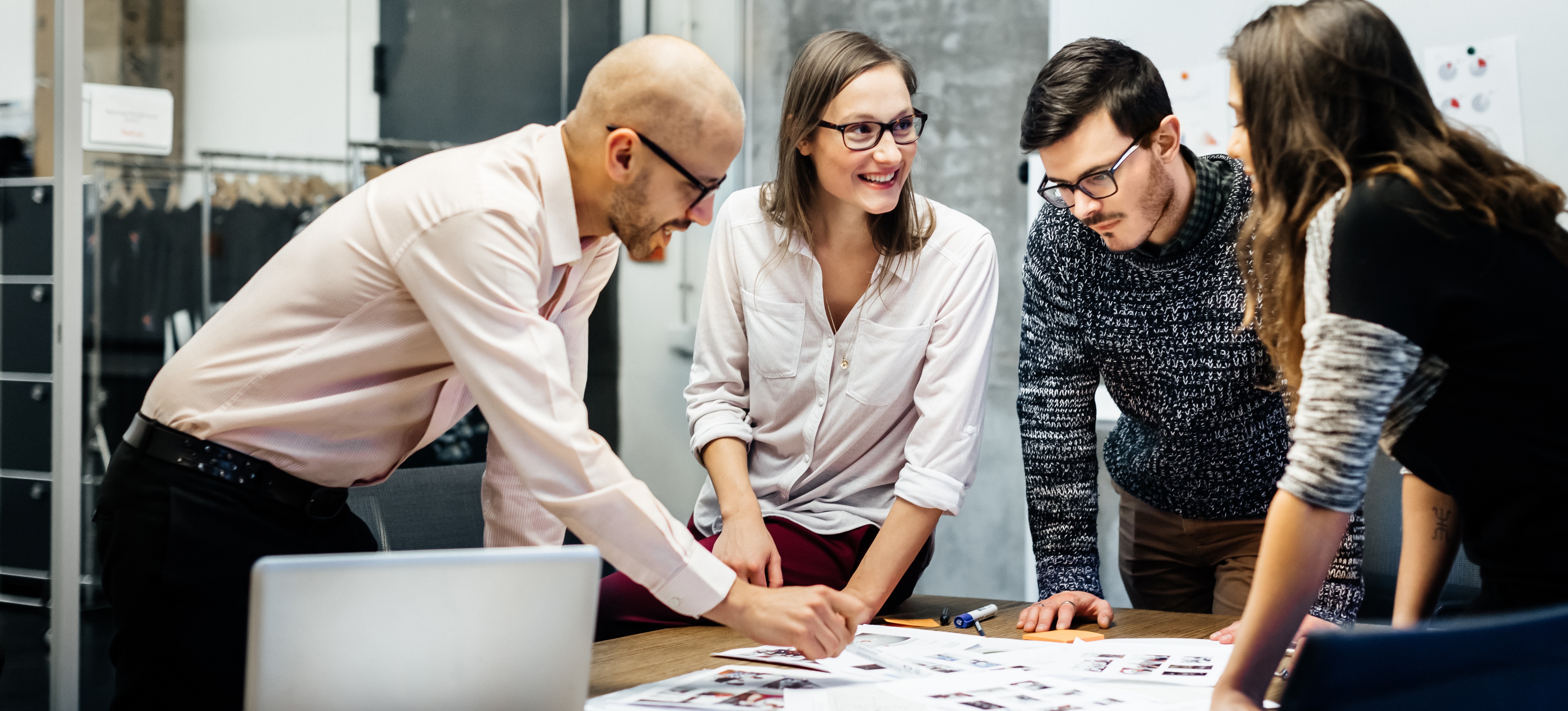[Featured Image] Each working on a digital marketing specialist salary, a group of four digital marketing specialists meets to discuss strategies, looking at an array of papers on a conference table in an office.