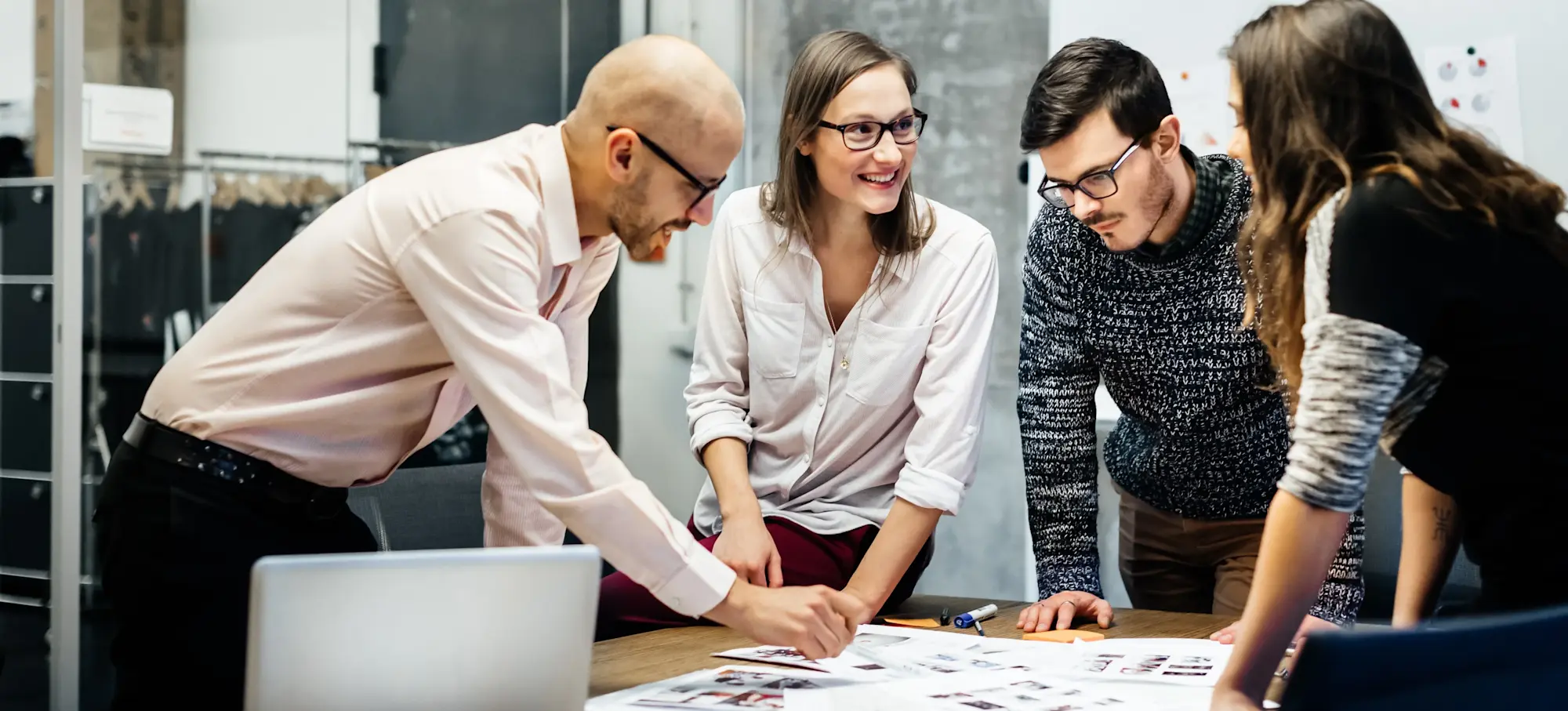 [Featured Image] Each working on a digital marketing specialist salary, a group of four digital marketing specialists meets to discuss strategies, looking at an array of papers on a conference table in an office.