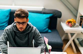 [Featured Image] A back-end developer in a gray sweatshirt uses their laptop to work on an API with nearby coworkers.